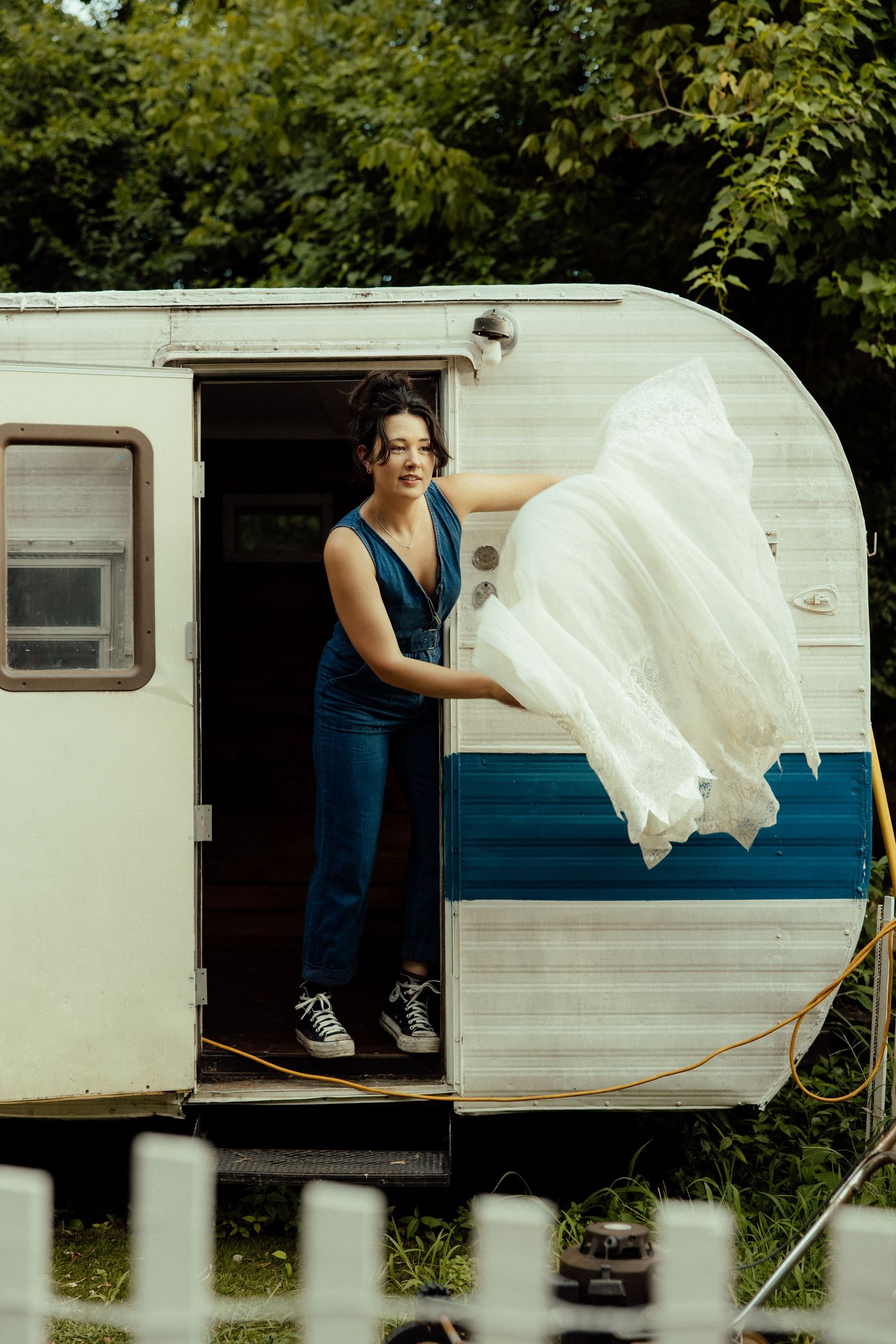 A vintage white and blue striped camper trailer with flowing white fabric in the doorway.