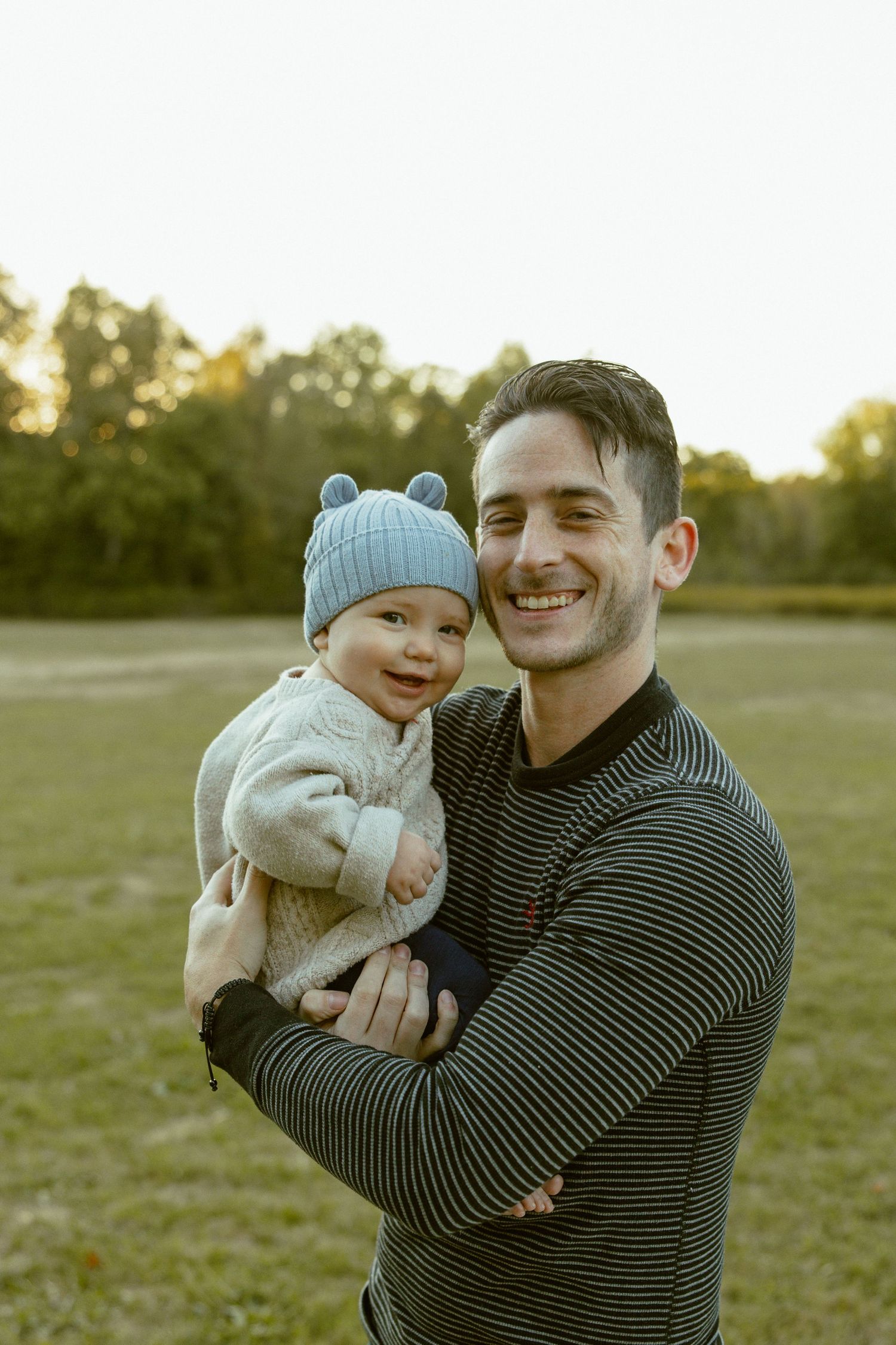 A parent and child share joyful moments together outdoors during golden hour in a grassy field.