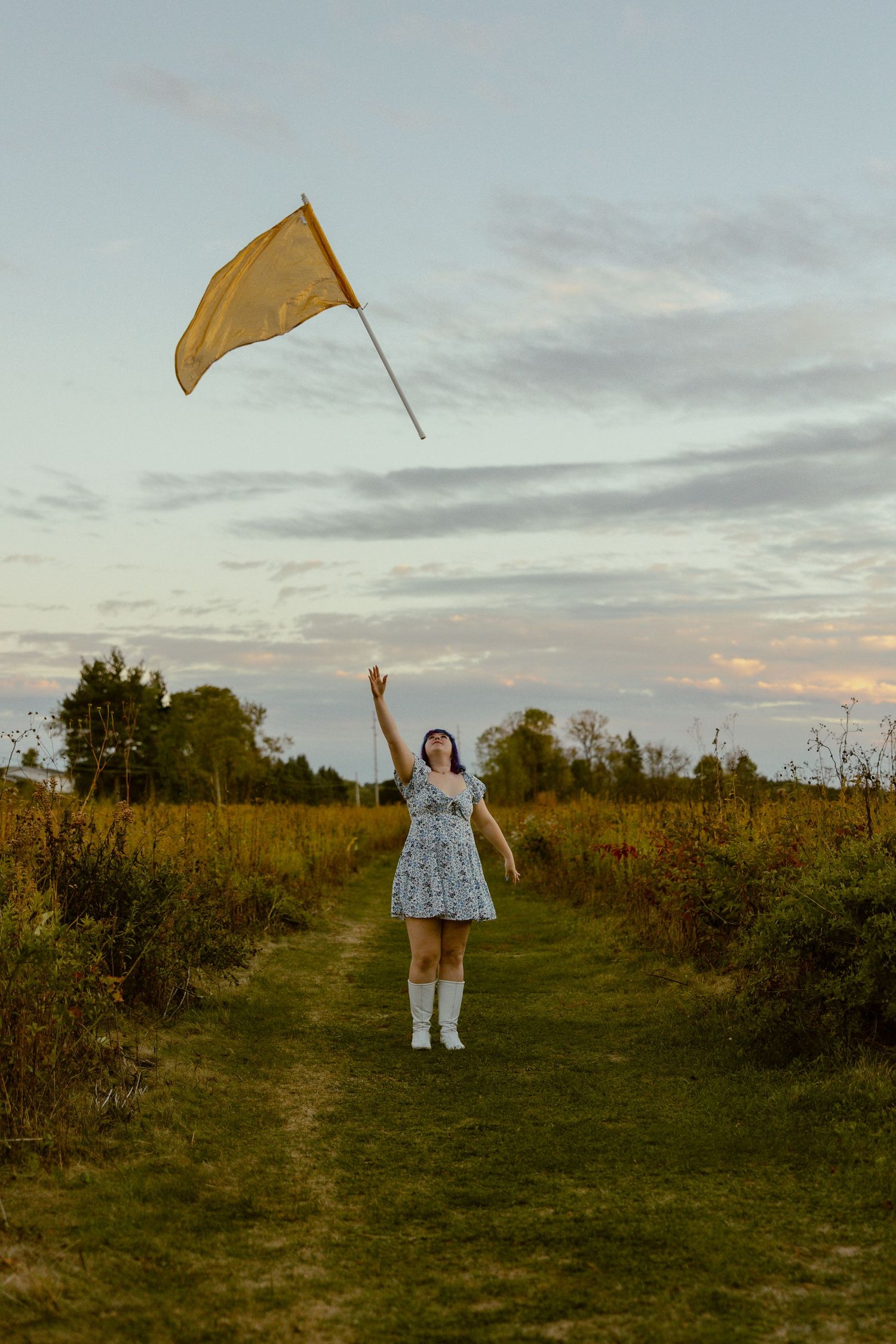 Two people stand in a grassy field at sunset while flying a golden kite in the warm evening light.