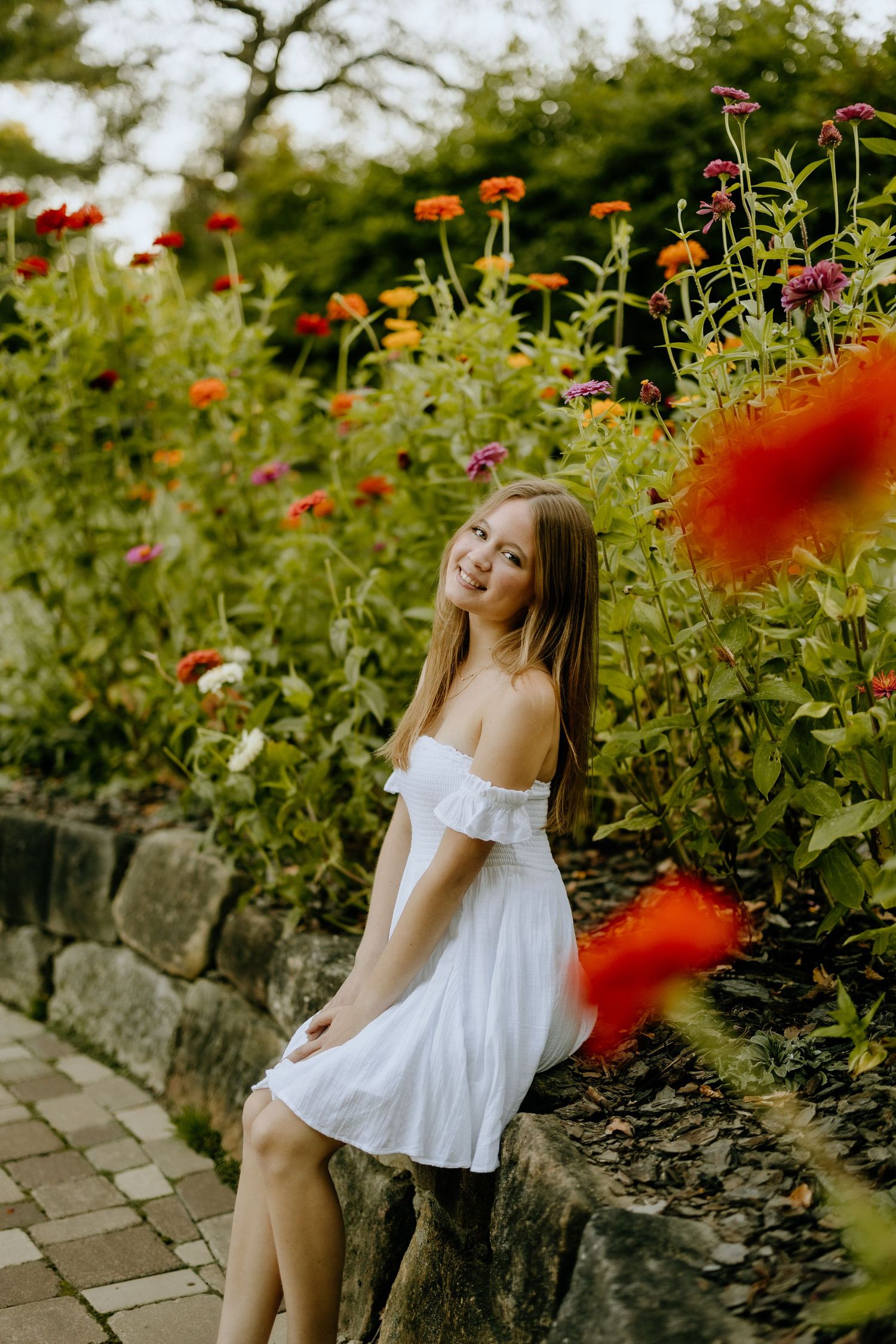 A white off-shoulder dress contrasts beautifully against vibrant orange zinnias in a garden setting.