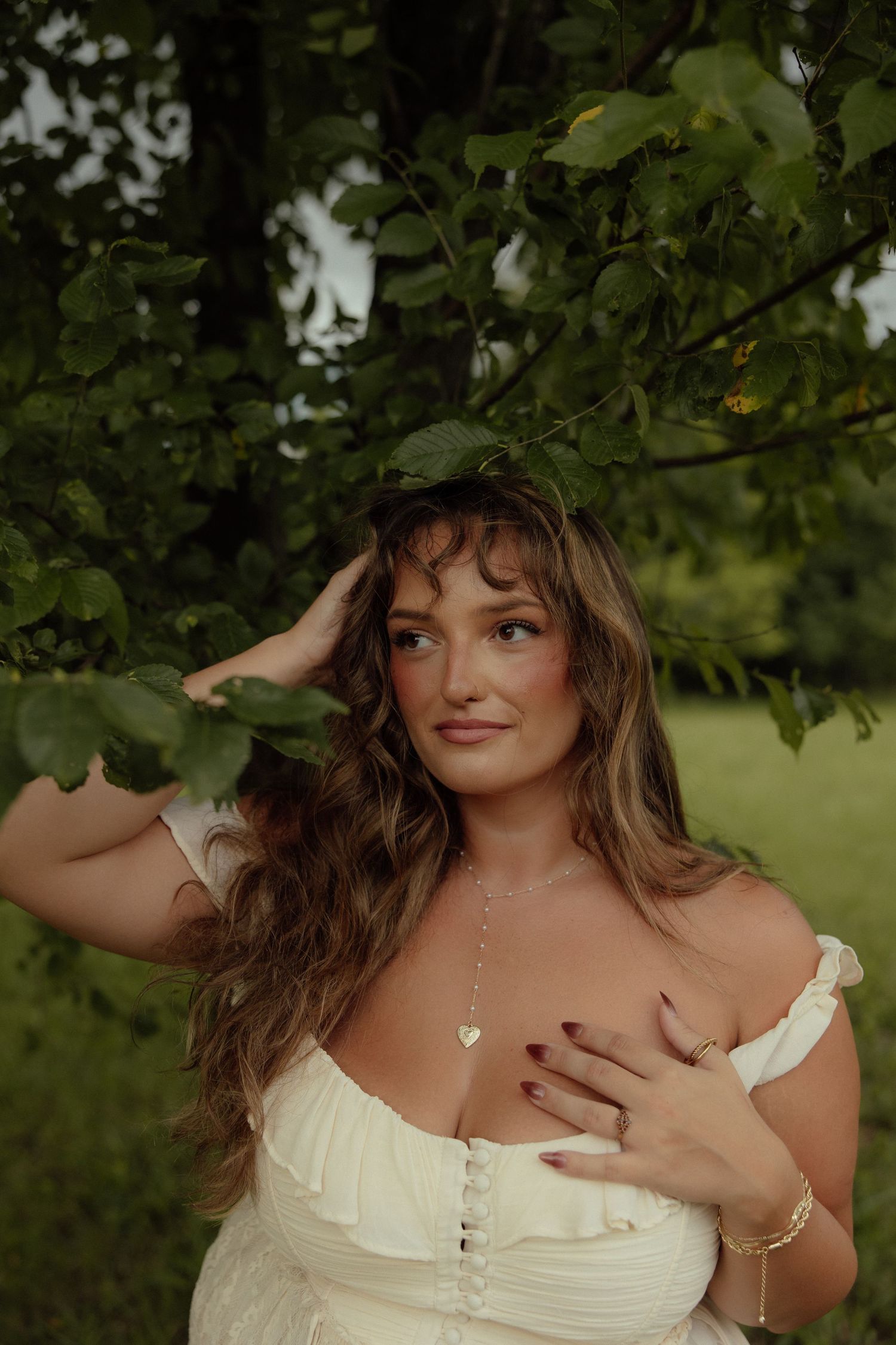 A person in a white ruffled dress poses in a garden setting with green foliage in the background.