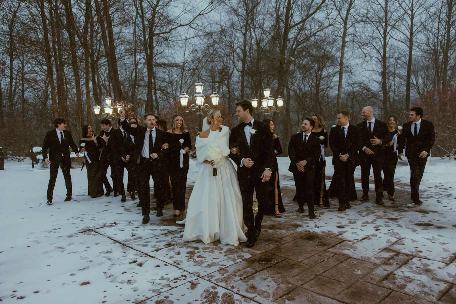 A winter wedding ceremony with guests gathered in the snow as a couple exchanges vows under decorative lights.