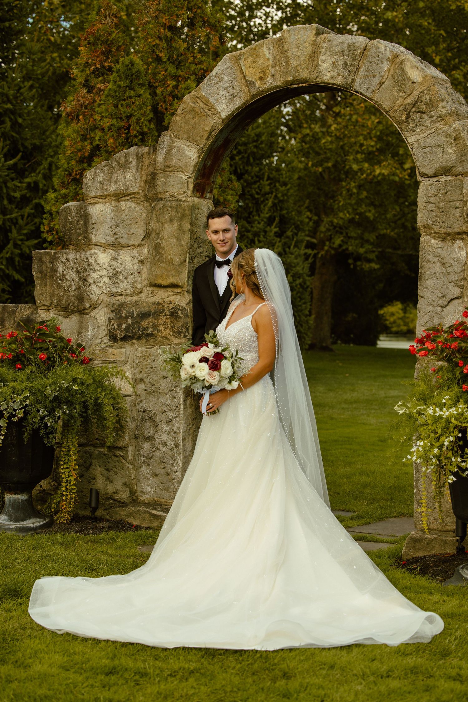 A romantic wedding photoshoot featuring a beautiful white gown against a stone archway in a garden setting.