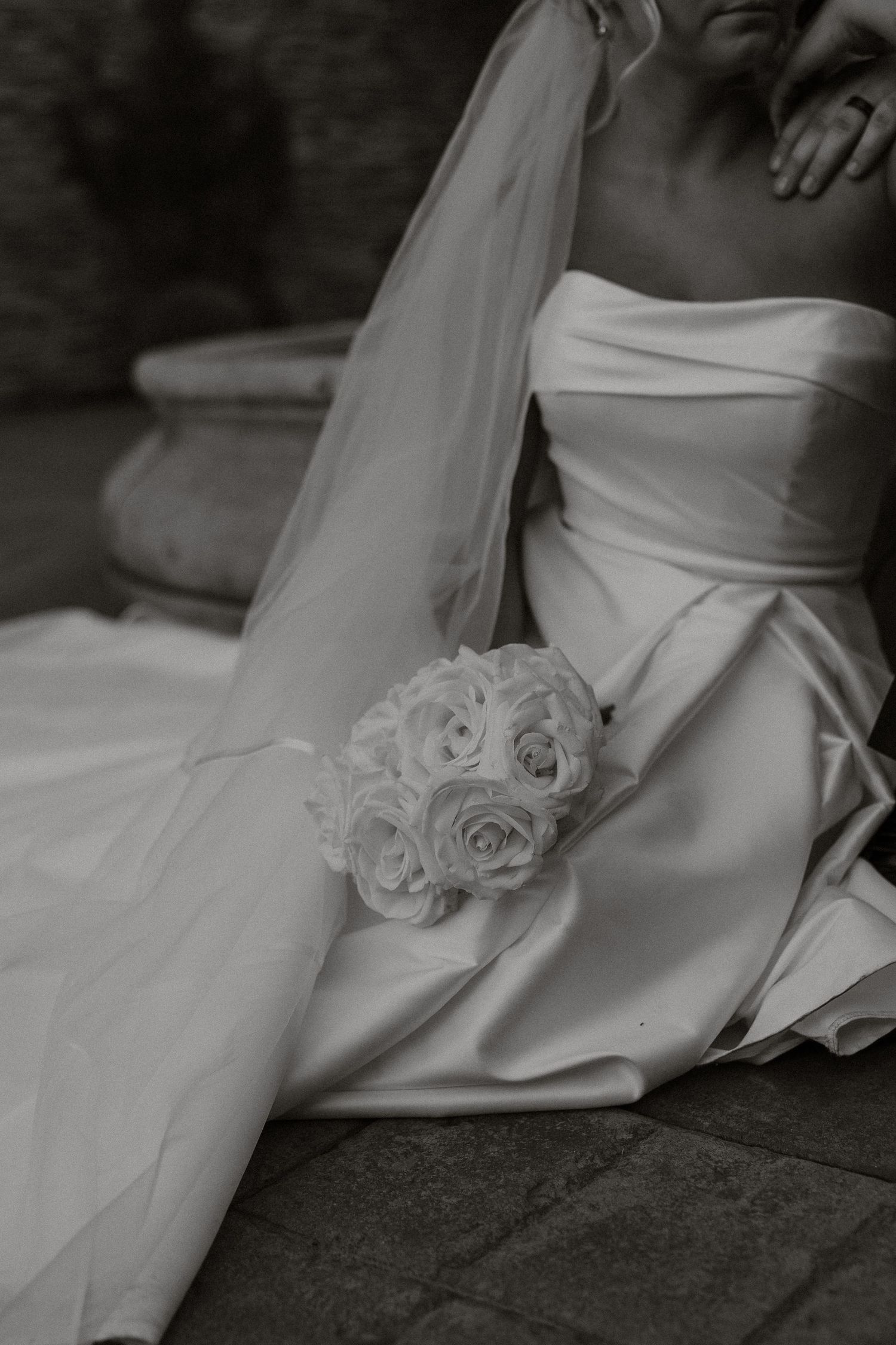 Close-up details of a white wedding dress with rose embellishments in dramatic black and white photography.