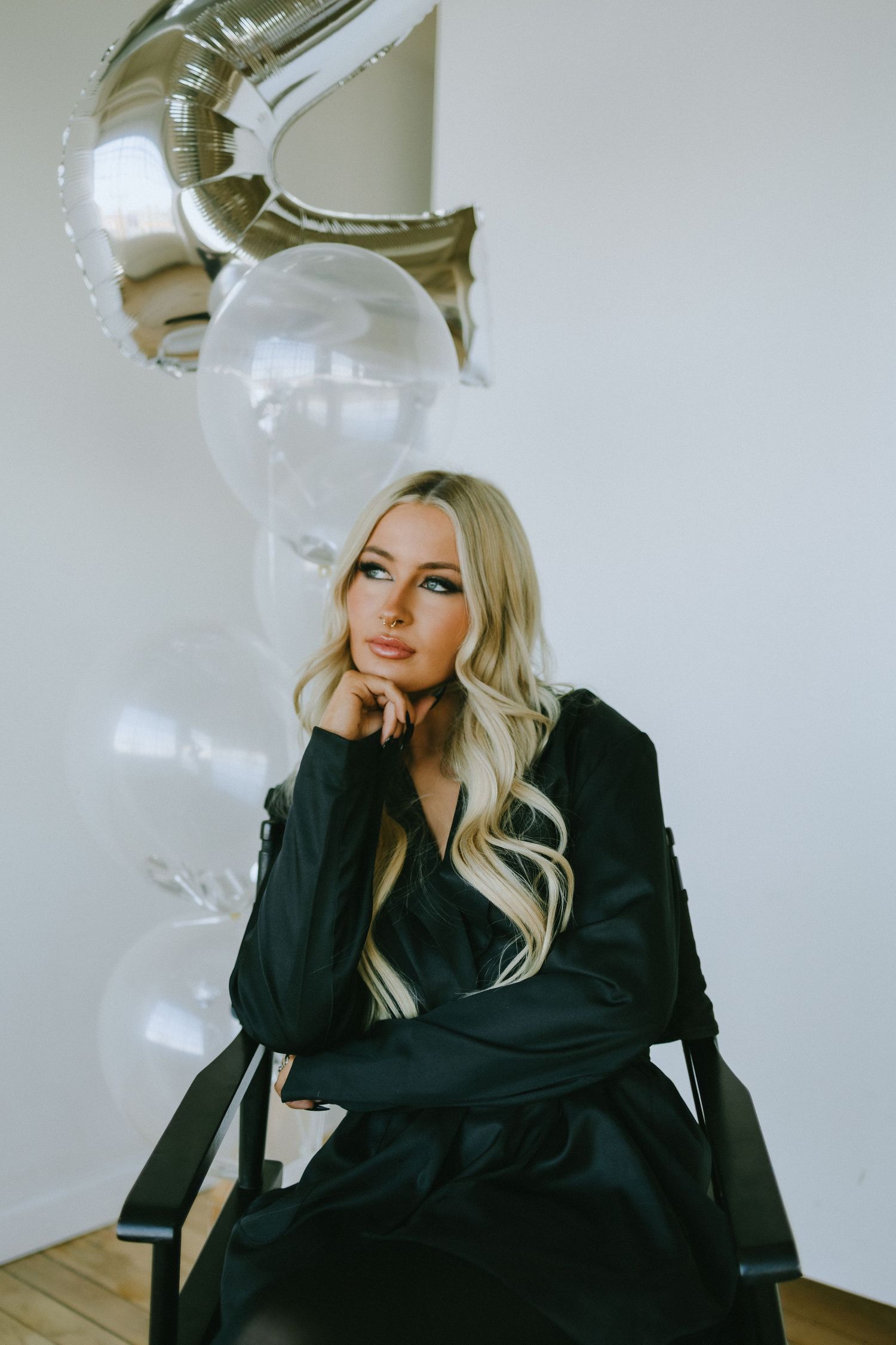 Person in black blazer poses thoughtfully with silver balloon and white balloon decor.