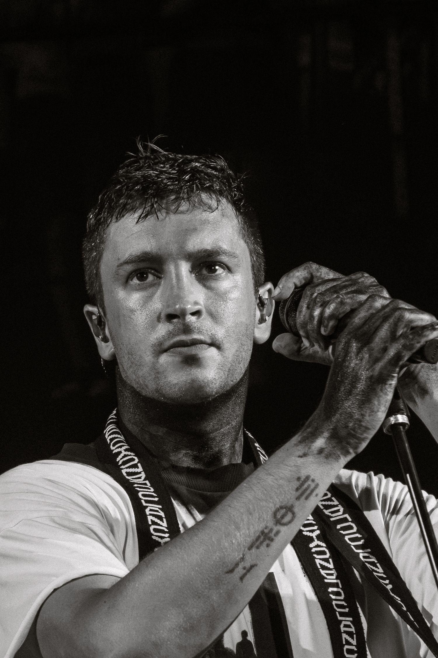 Black and white portrait of performer with tattoos holding microphone during concert.