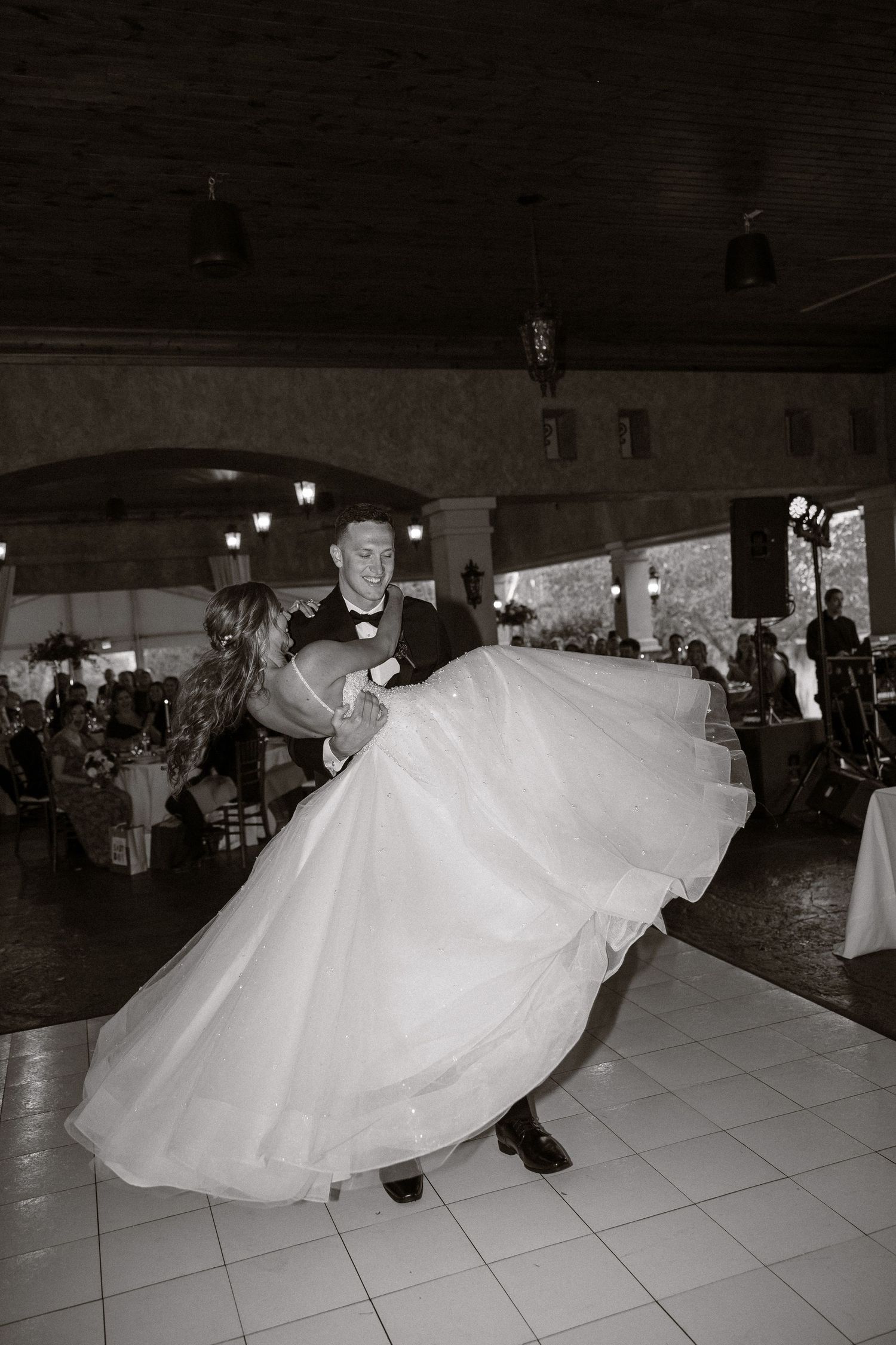 A dramatic black and white photo of newlyweds performing their first dance on a reception floor.