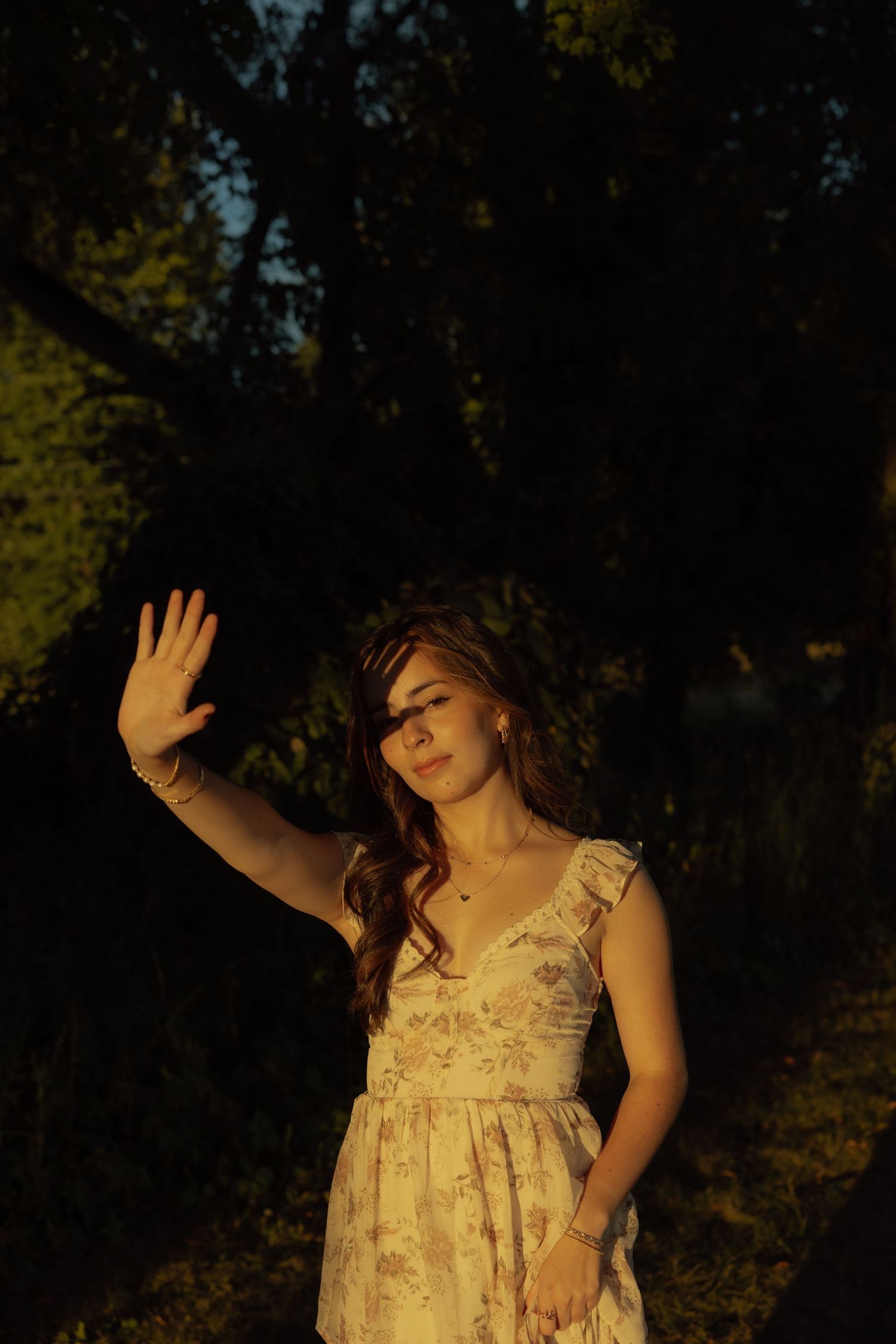 A person in a floral dress poses expressively against a dark forest backdrop in a series of artistic shots.
