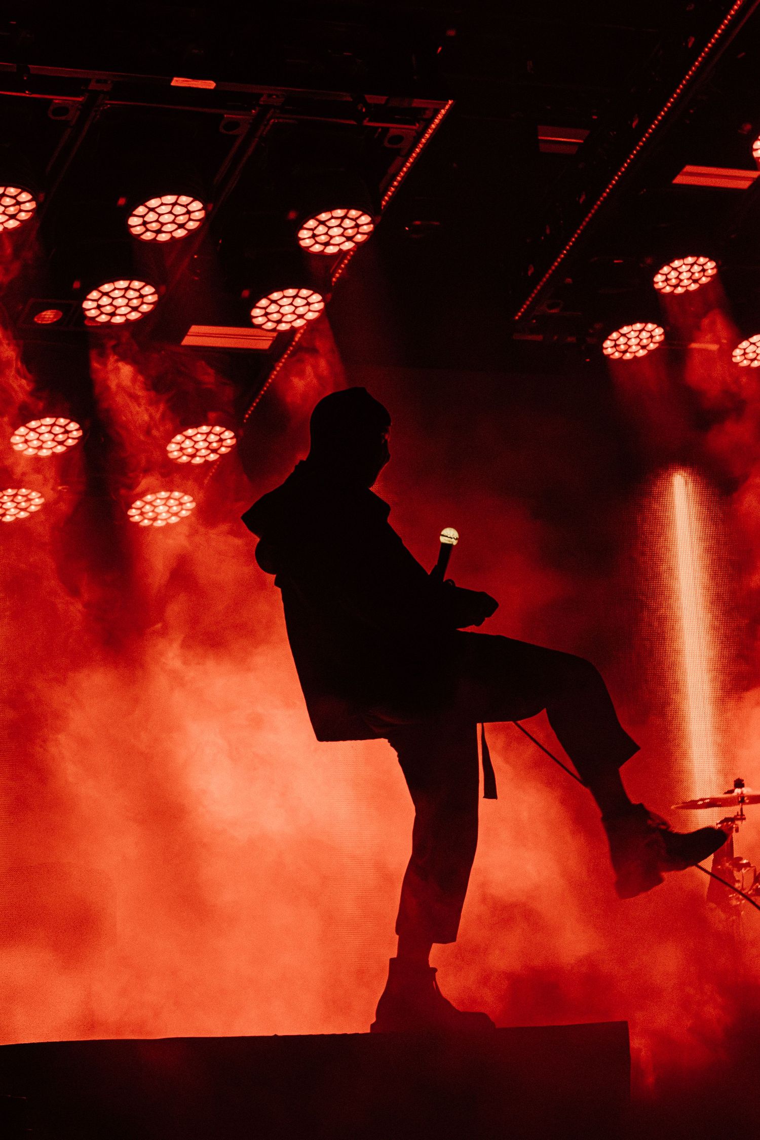Silhouetted performer in dynamic pose against red stage lighting and smoke effects.