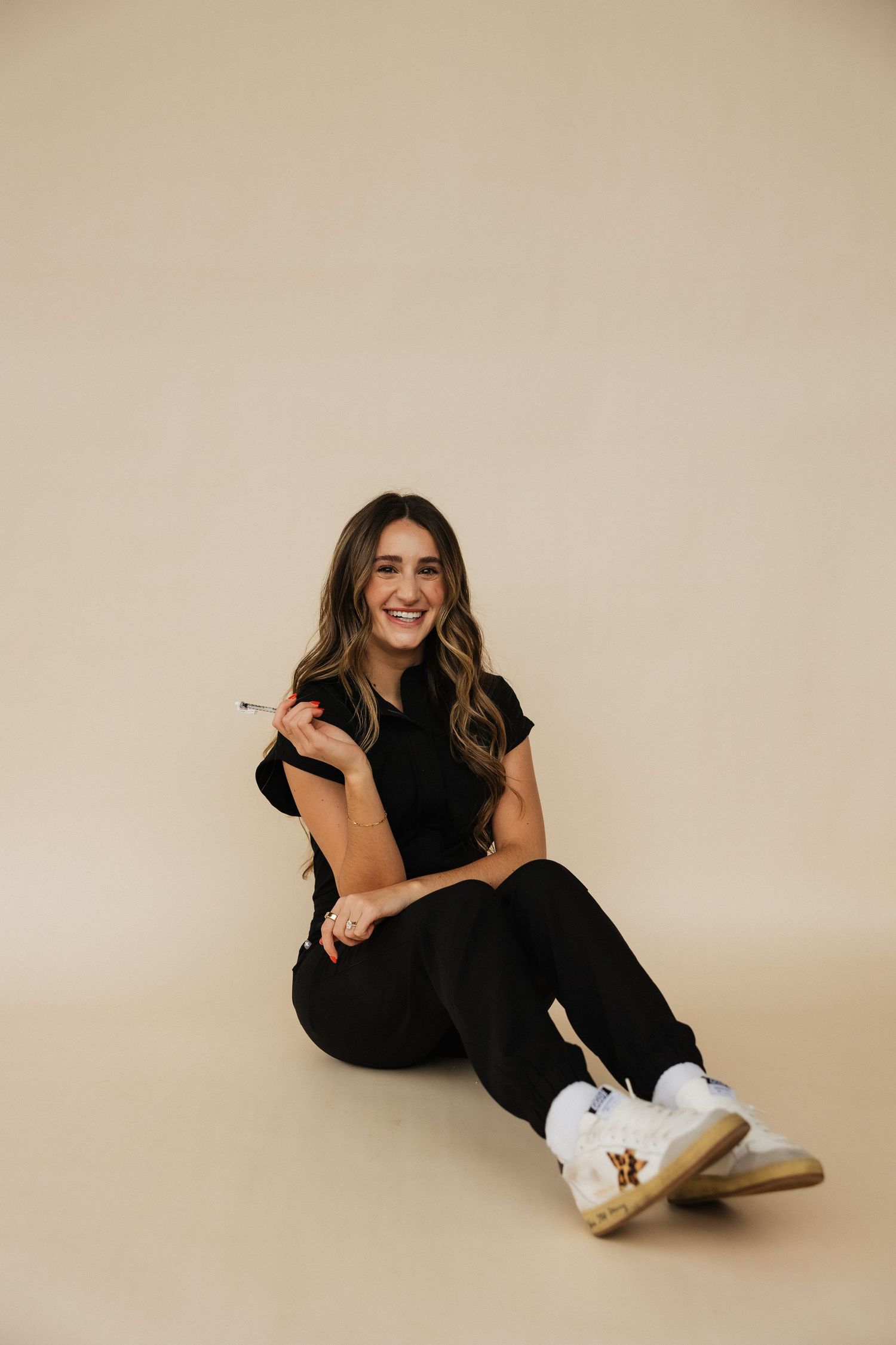 Casual portrait of woman sitting on floor wearing black outfit and white sneakers.