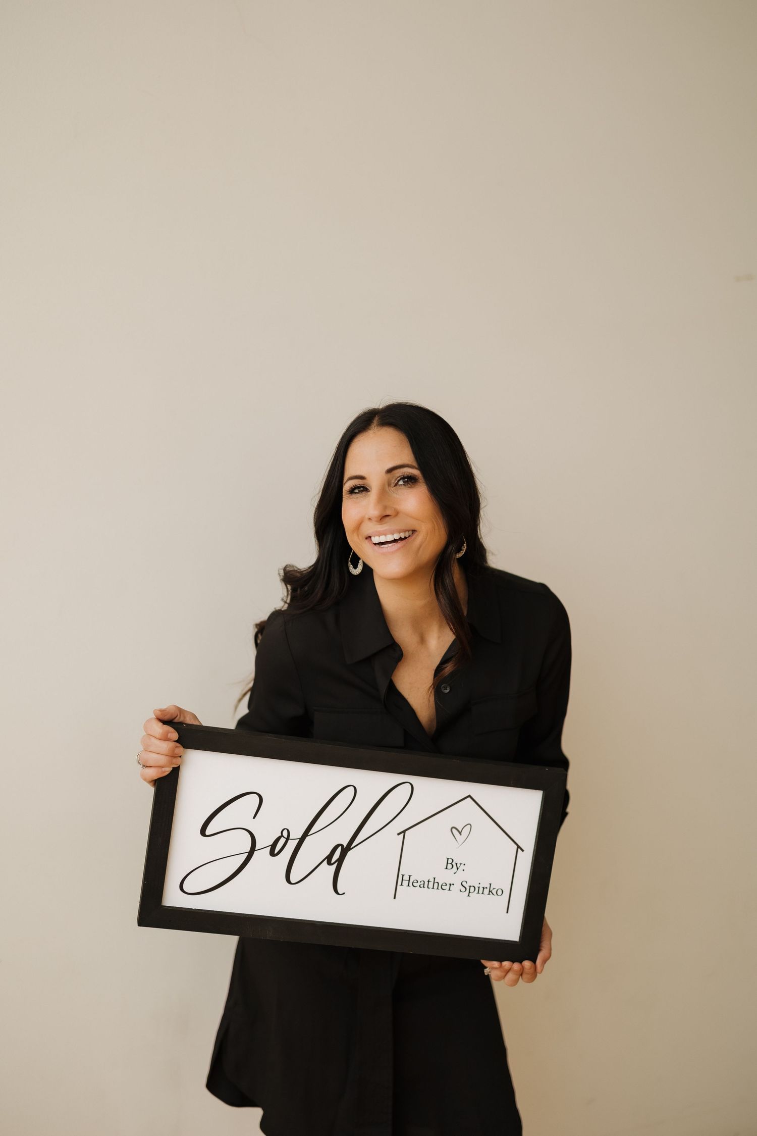 Business professional holding sign in black outfit against beige background.