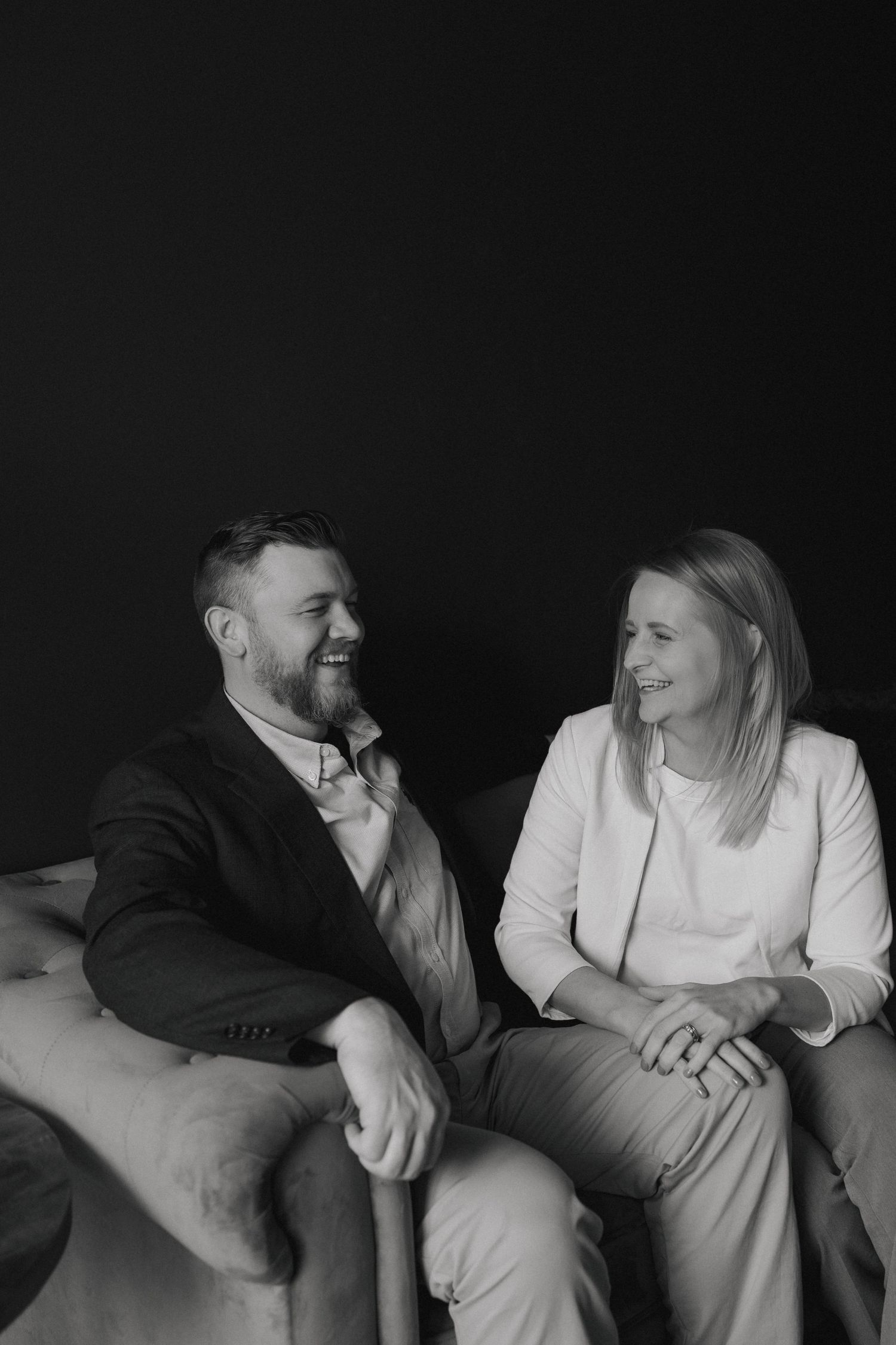 Two professionals sharing conversation while seated on gray couch in black and white photo.