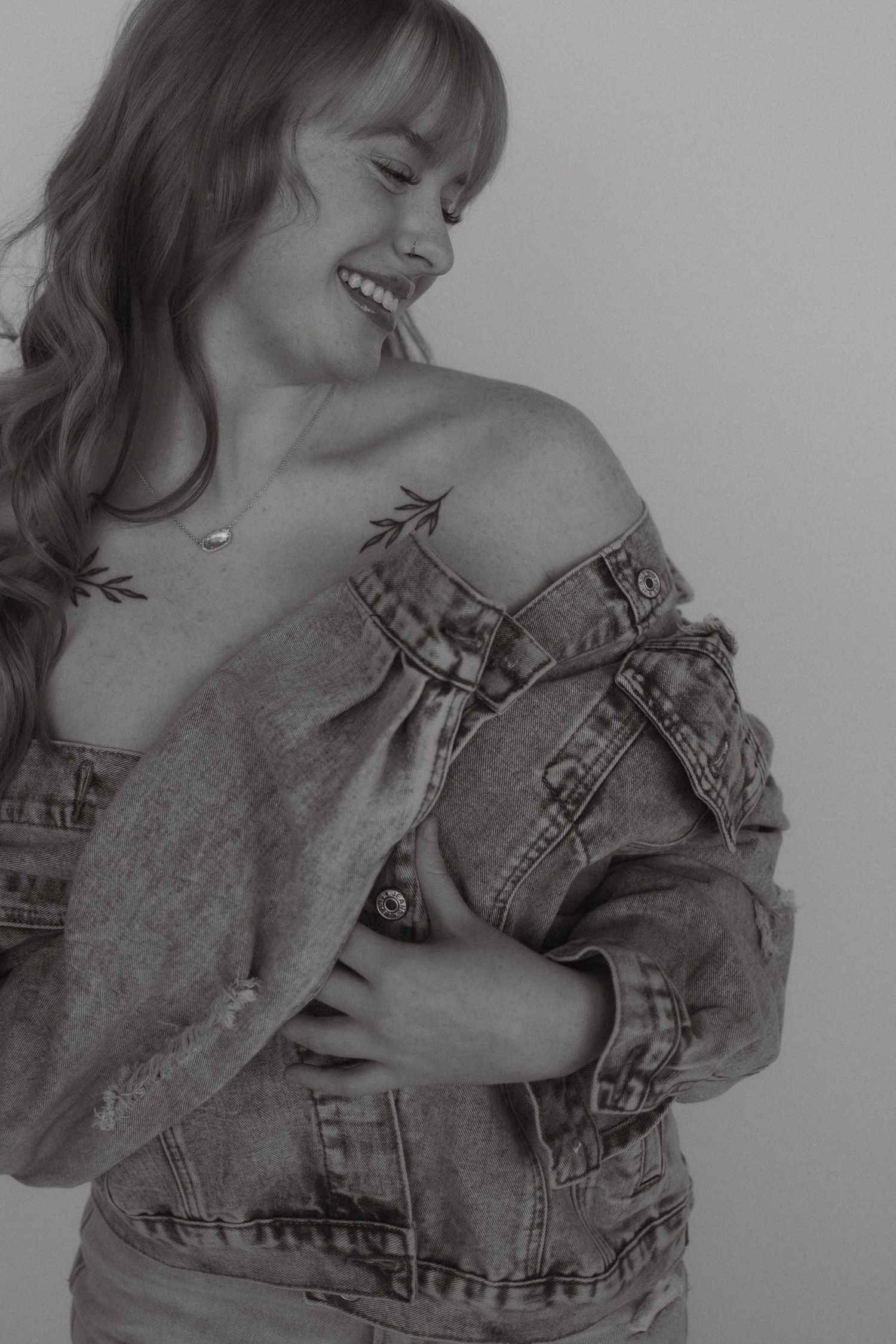 Black and white portrait showing joy while wearing an off-shoulder denim jacket.