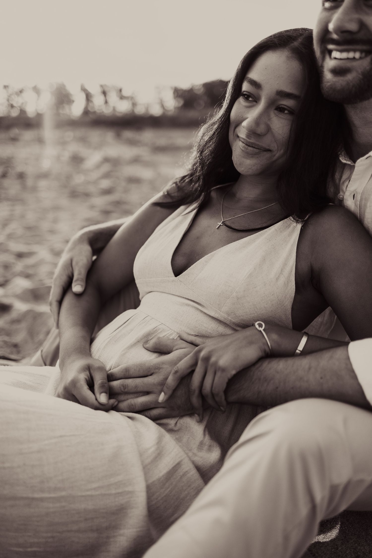 A loving couple embraces on the beach during a maternity photoshoot.