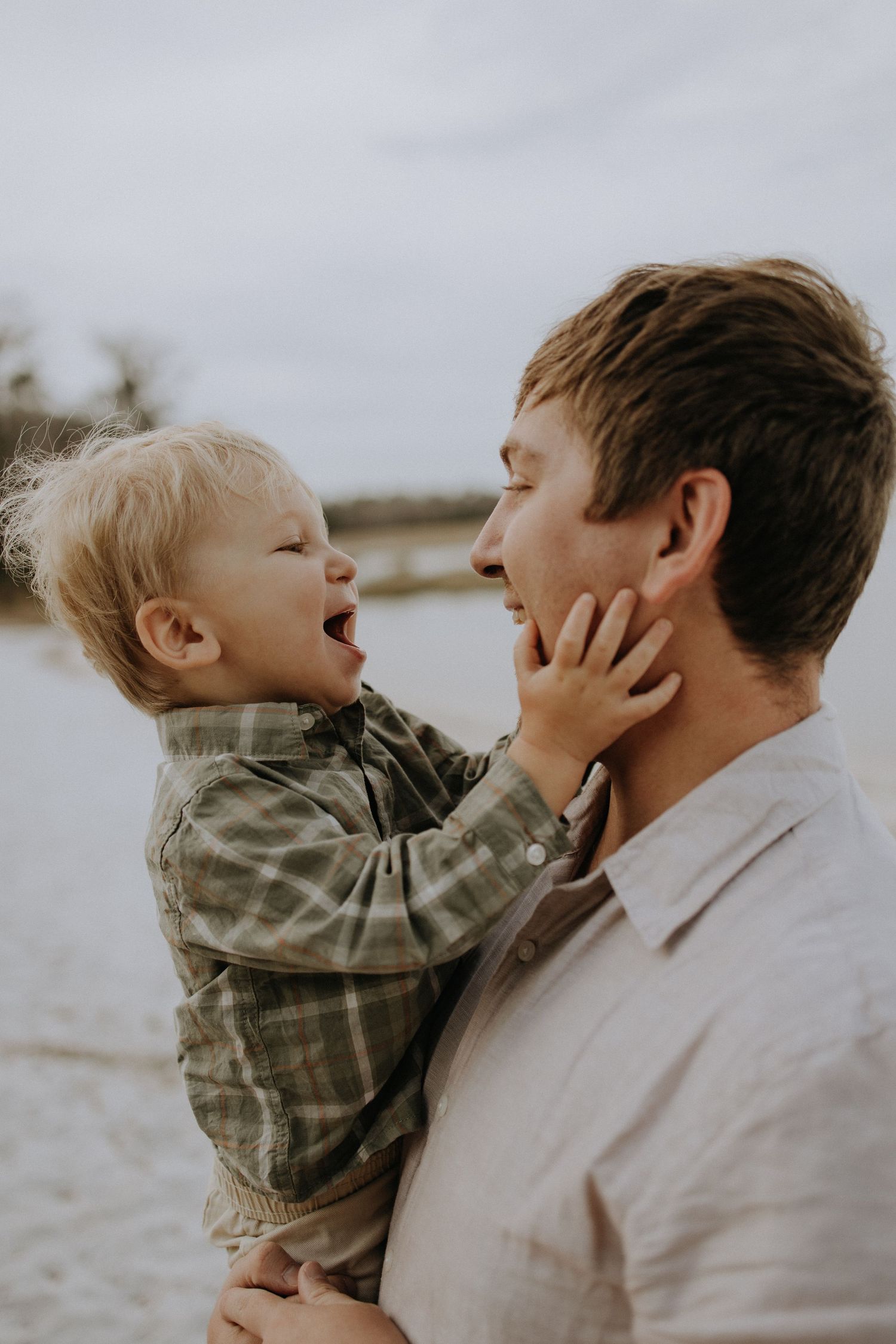 A joyful moment shared between a parent and small child on a beach during an overcast day.