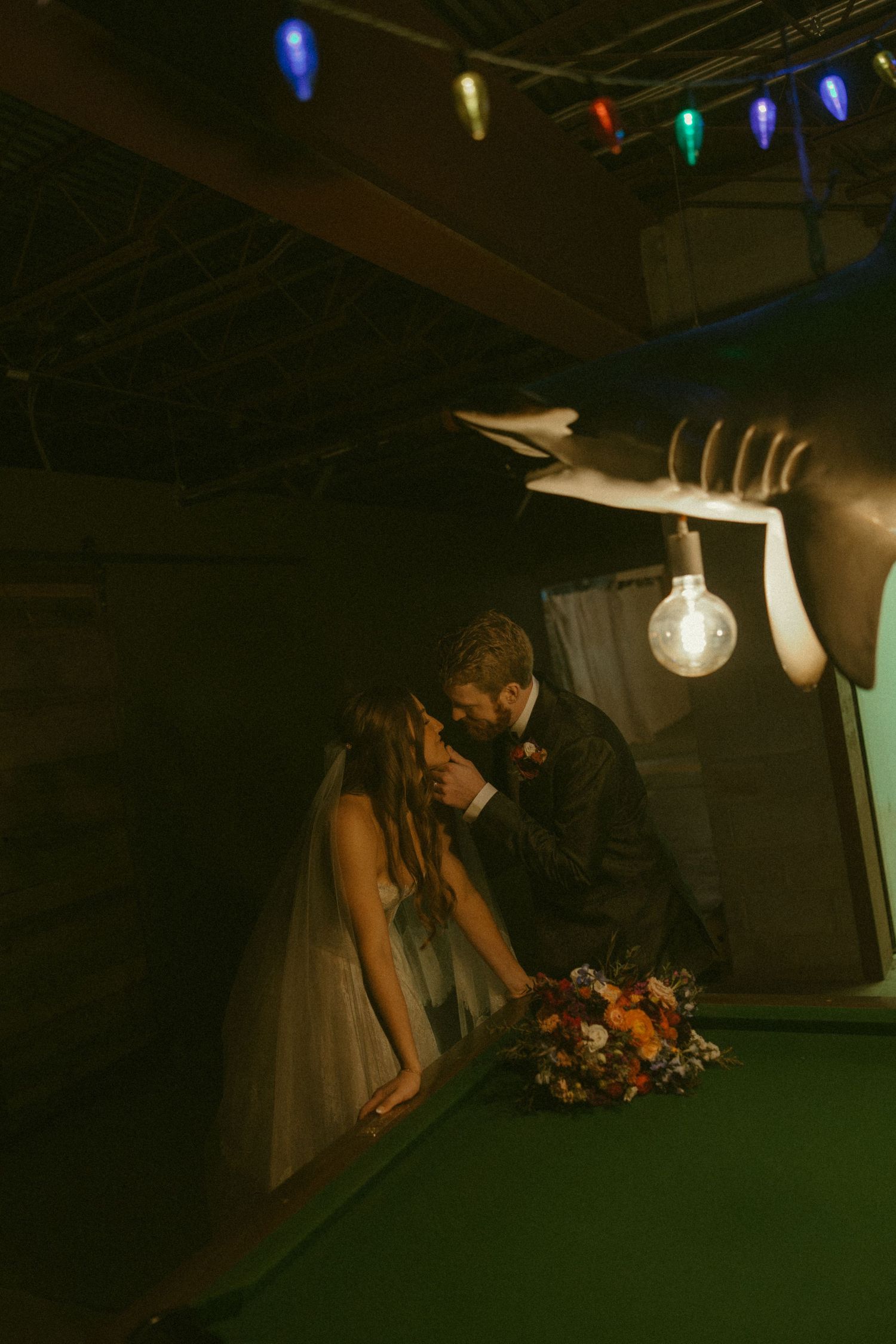 A romantic wedding couple shares intimate moments under twinkling lights at dusk.