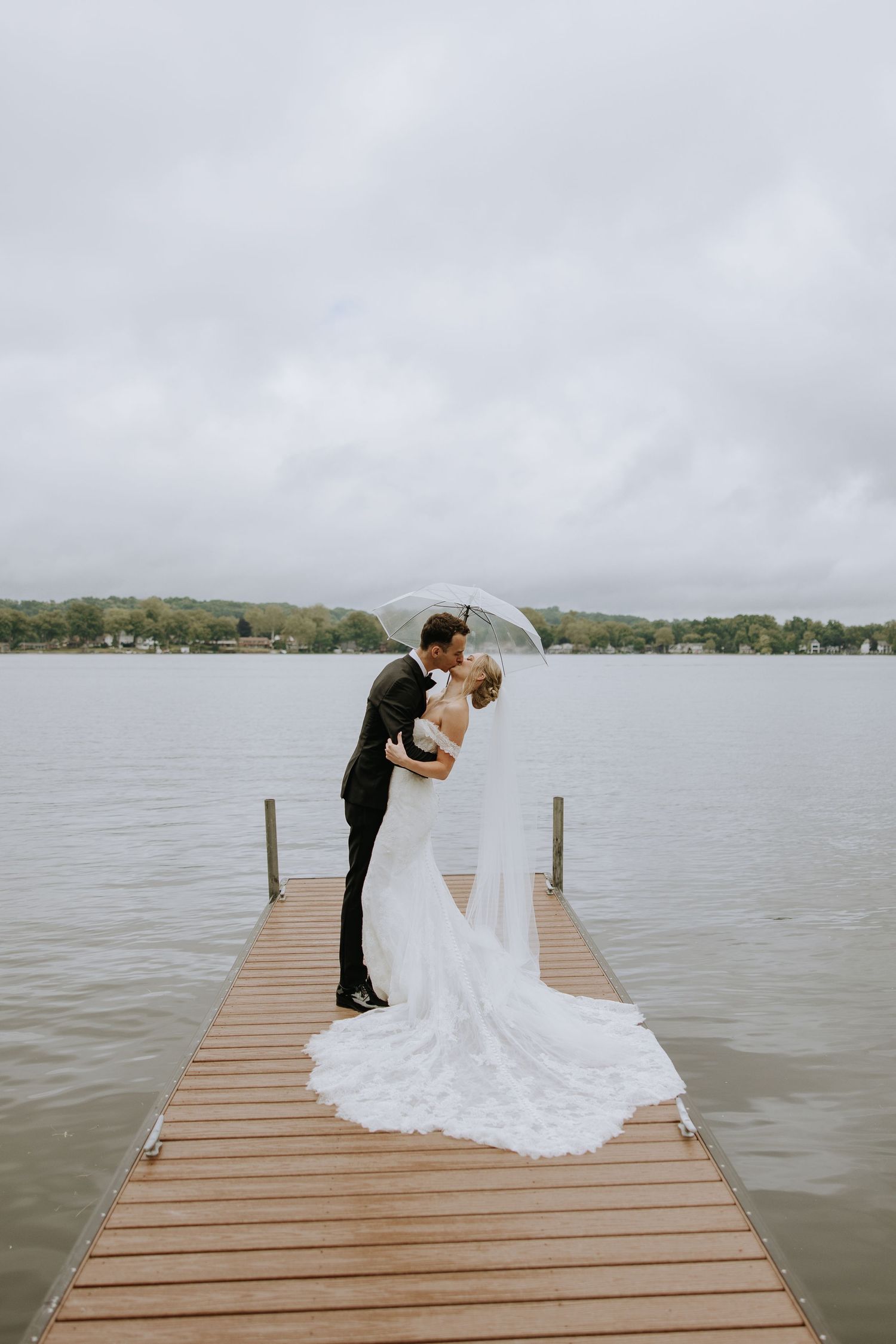 Romantic moment on a wooden dock over a lake with flowing white wedding dress.