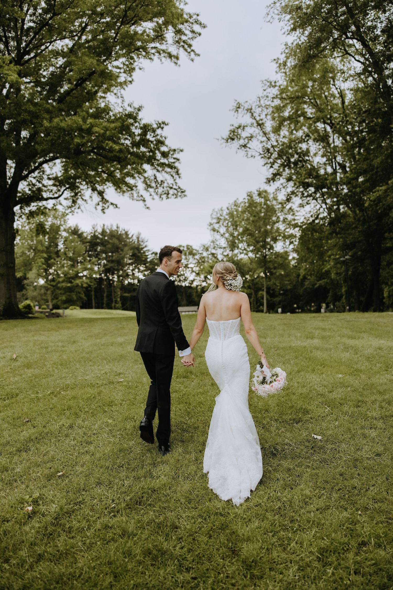Couple walking hand in hand across a lush green lawn on their wedding day.