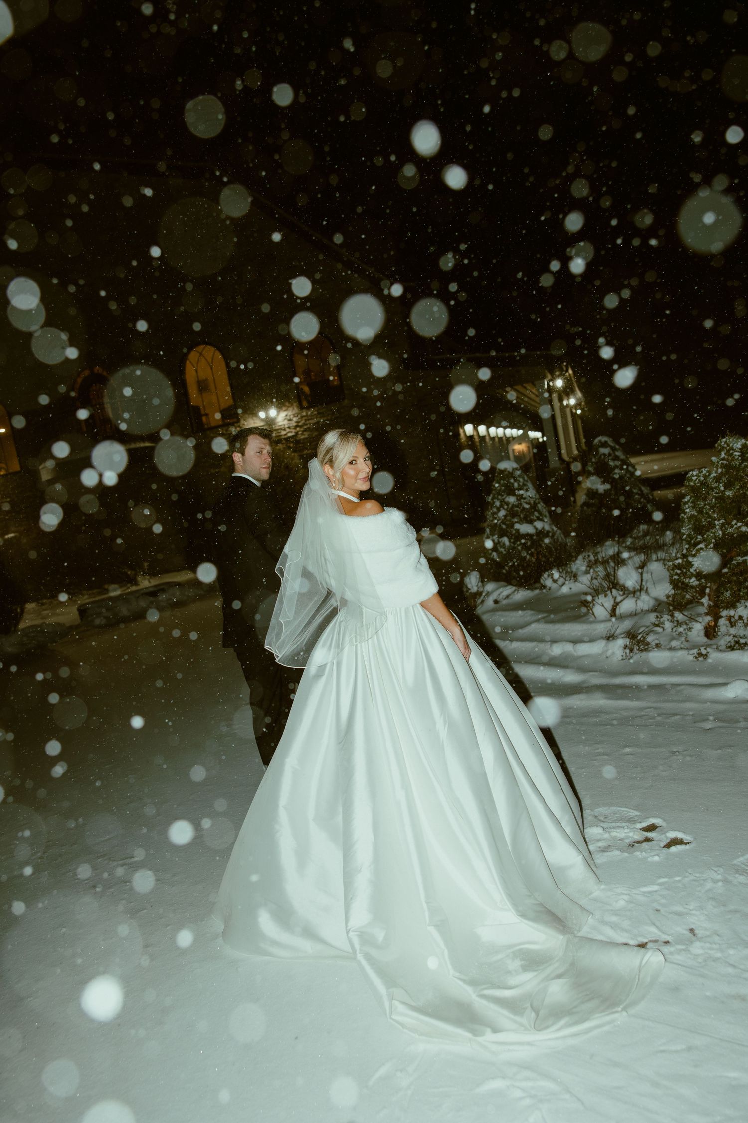 A bride in a flowing white dress poses in the snow during a magical winter photoshoot.