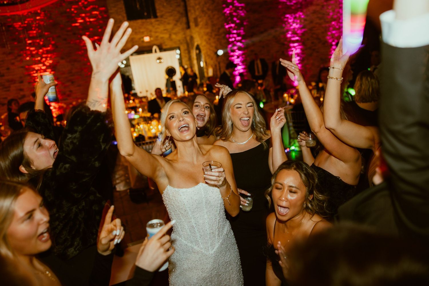Wedding reception dance party with colorful uplighting and guests celebrating on dance floor.
