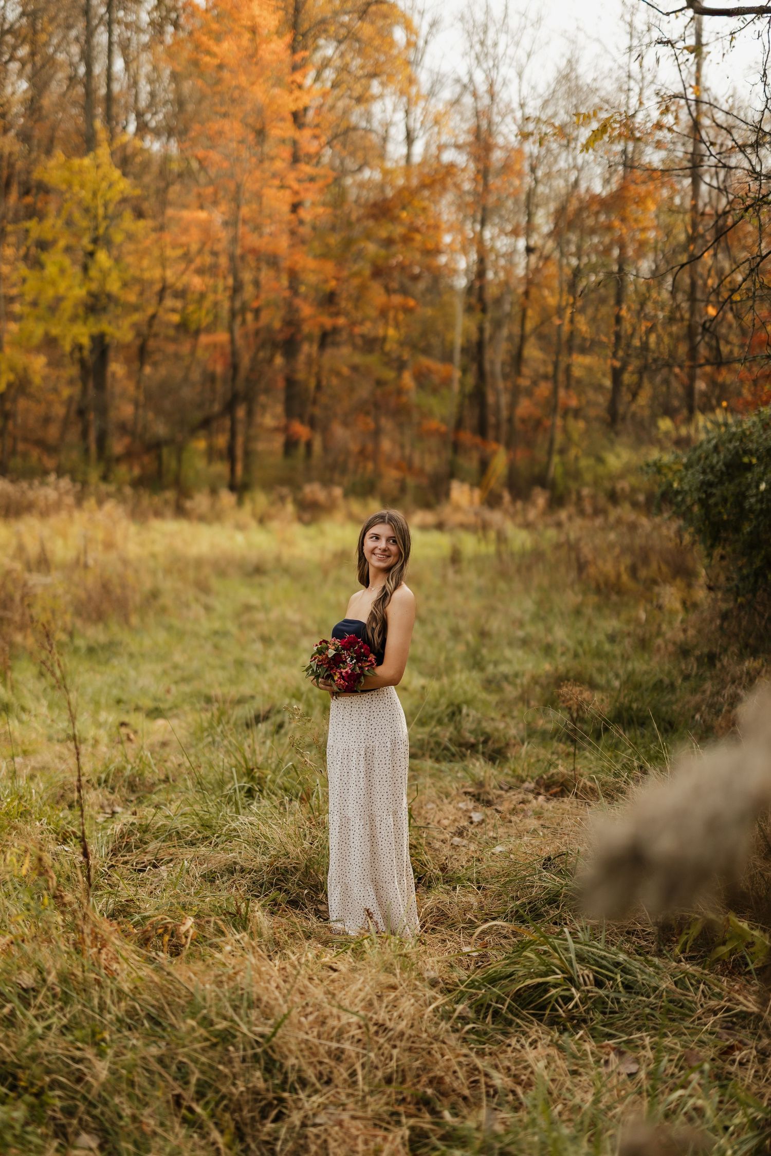 A long white dress stands out against the warm autumn colors of a wooded field.