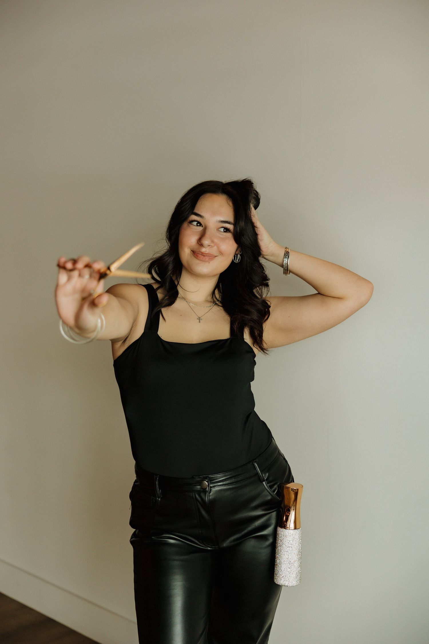 Casual portrait in black tank top with hair styling tools against neutral wall.