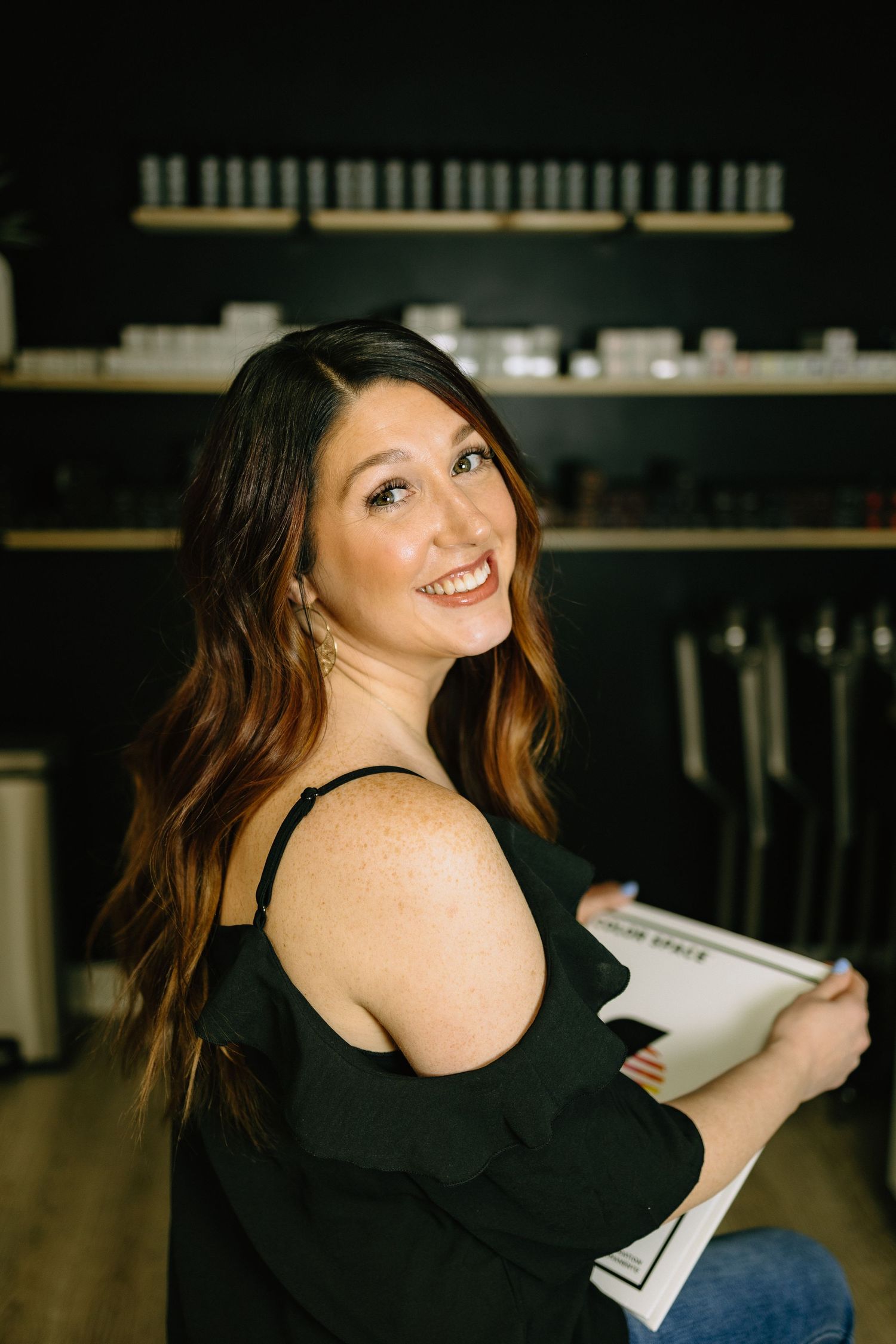 Person in black off-shoulder top holds paperwork in retail space with shelving.