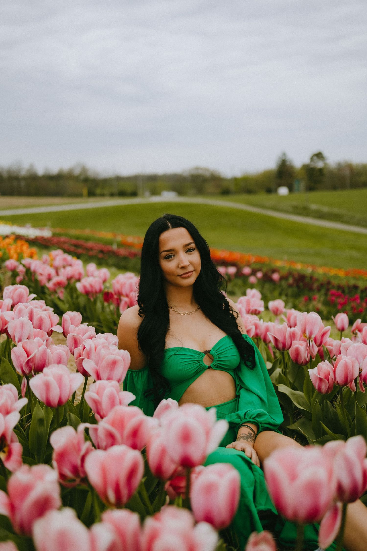 Portrait in emerald green dress surrounded by pink tulips in a spring garden.
