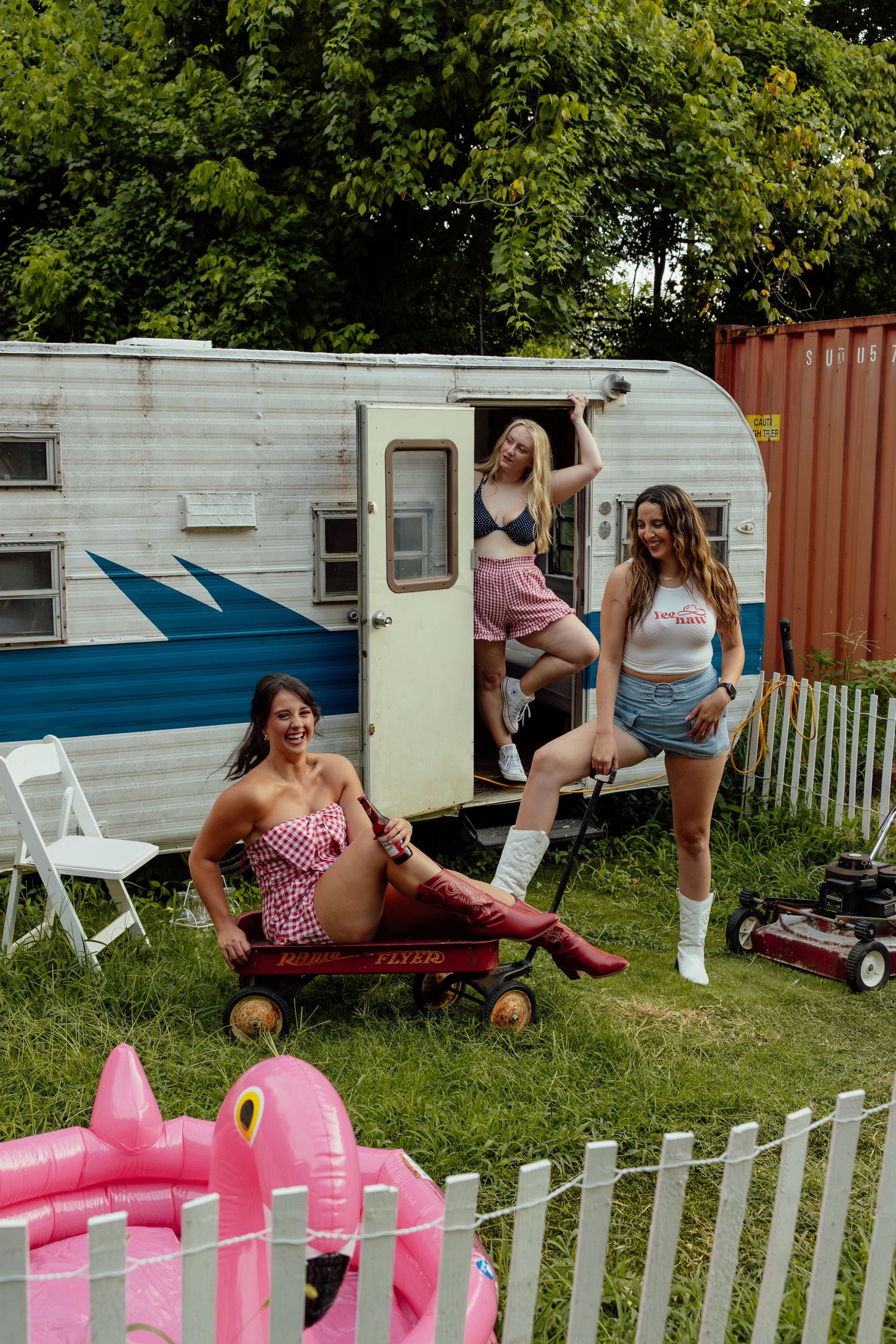 Five vintage travel trailers parked in a row with a white picket fence and pink lawn flamingos in the foreground.