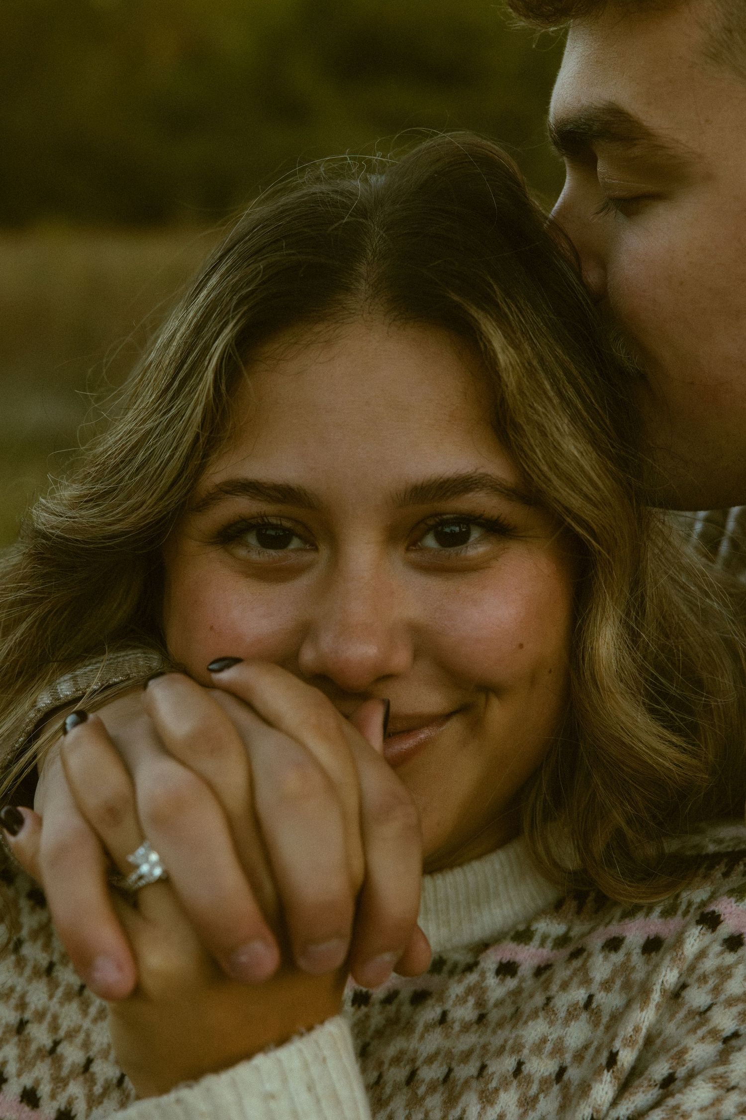 A close-up series of someone smiling and covering their mouth with their hand in a cozy sweater.