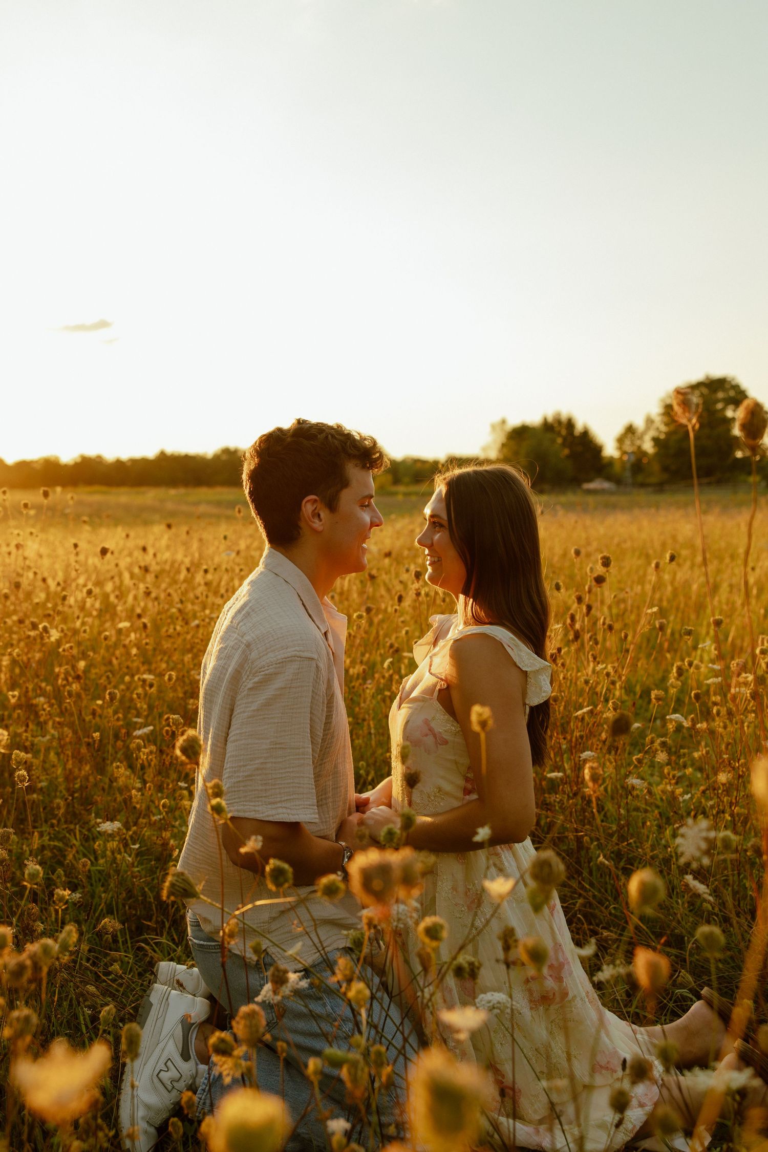 Two people sitting together in a golden wildflower field at sunset sharing an intimate moment among blooming flowers.