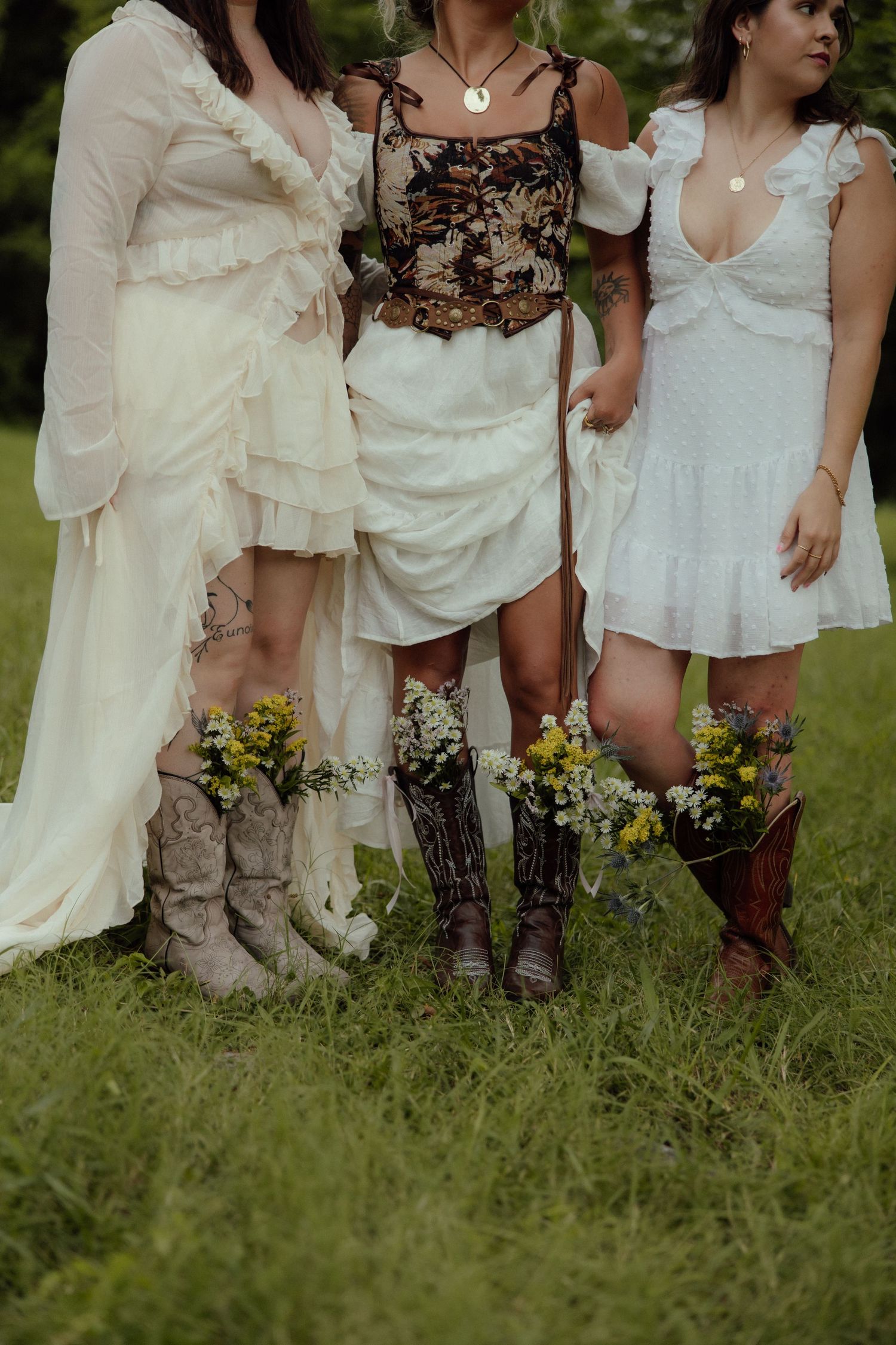 Close-up view of cowboy boots worn with white dresses showing a rustic country wedding style in an outdoor setting.
