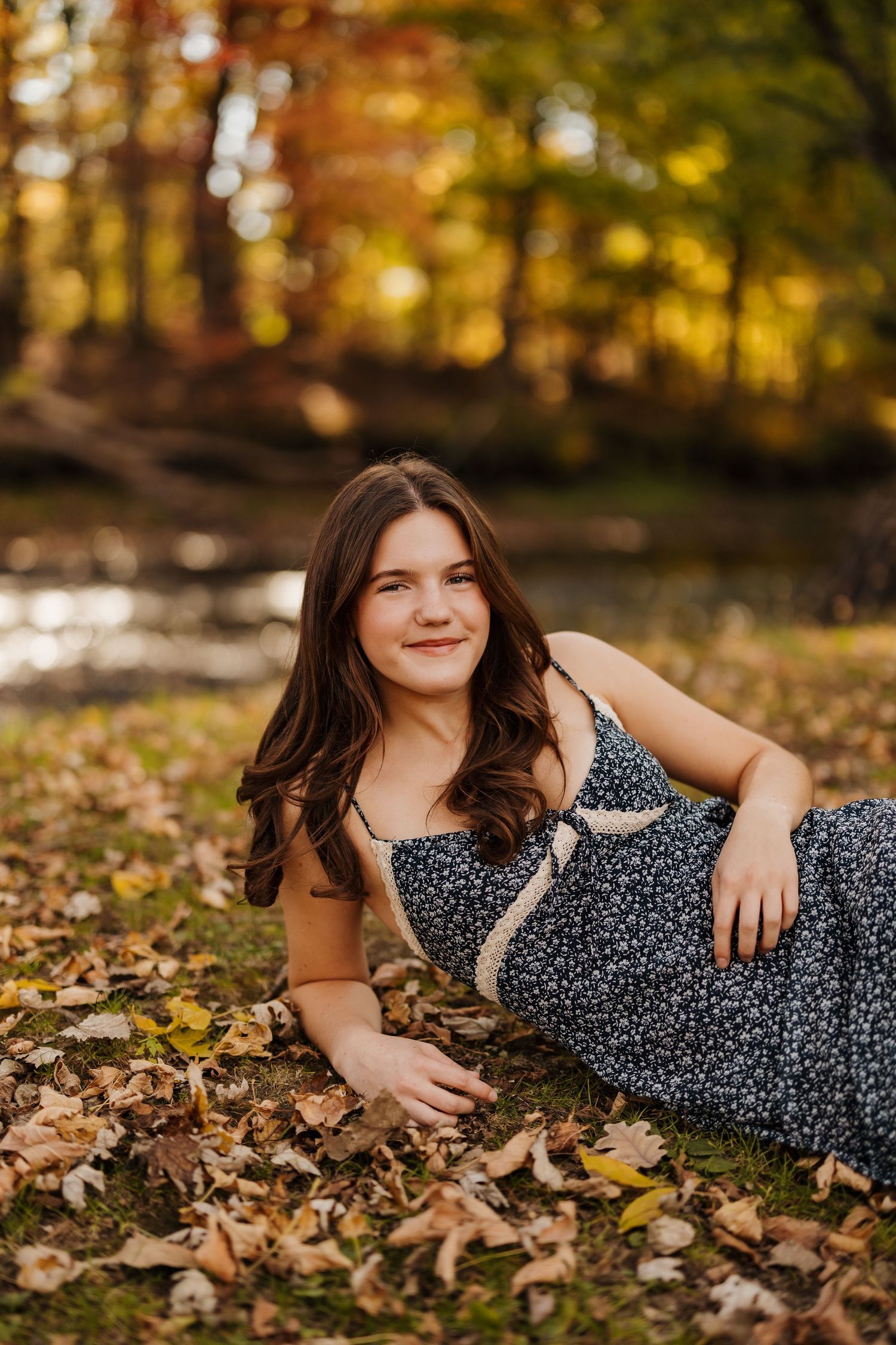 A beautiful autumn portrait session by a creek with fallen leaves and golden trees in the background.