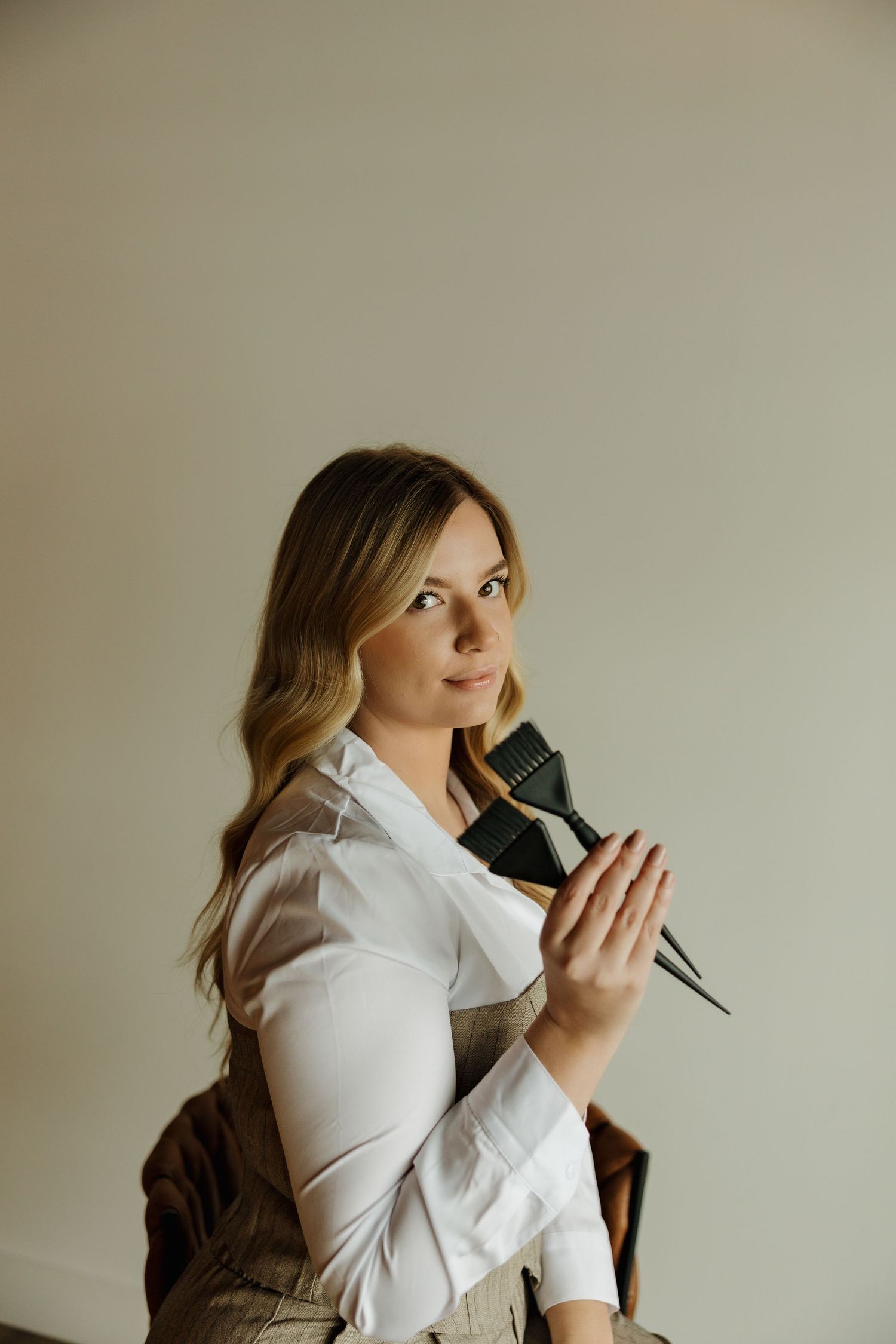 Professional portrait with white blouse and beige vest holding microphone against neutral background.