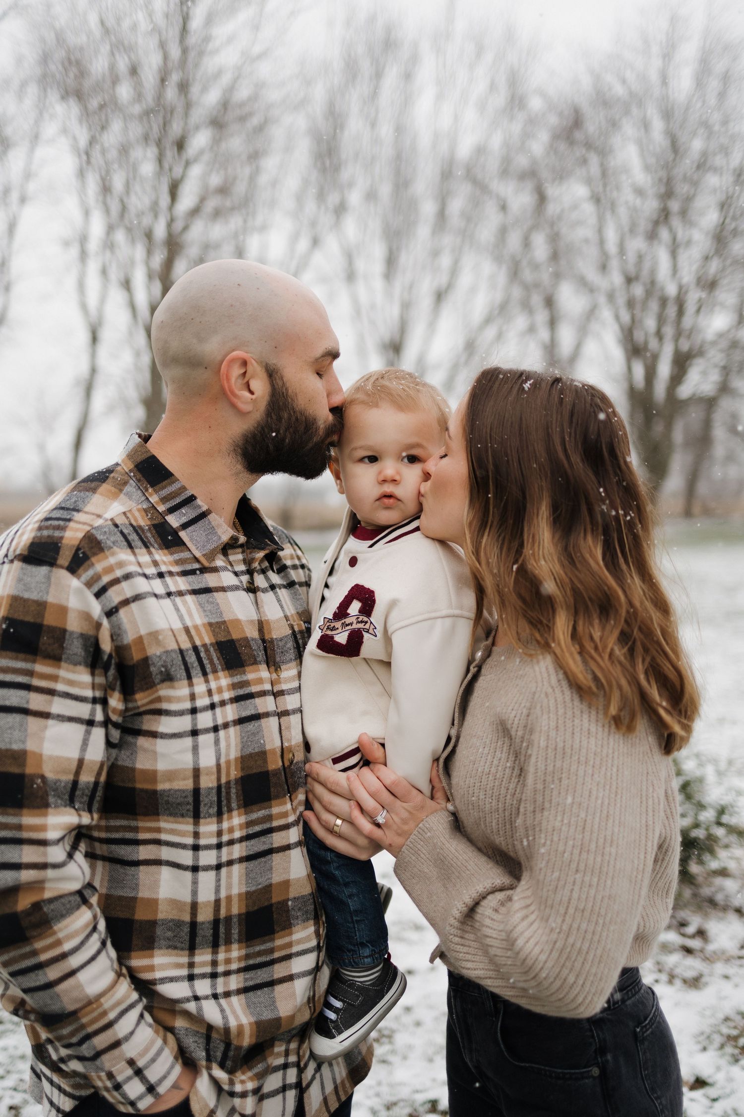 Family cuddles together in winter scene with plaid shirt and sweater.