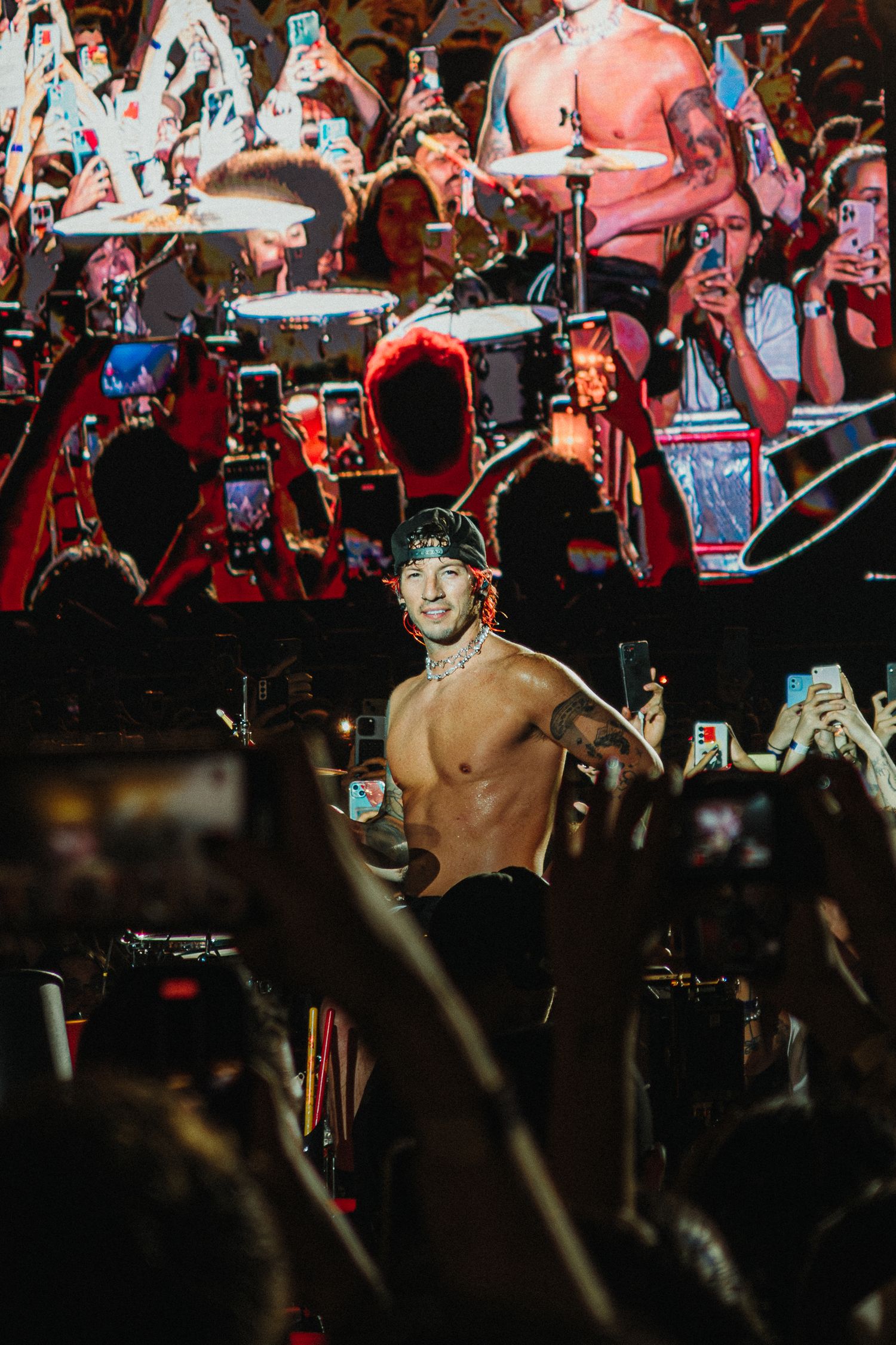 Concert performance with video screens and crowd holding up phones in red lighting.