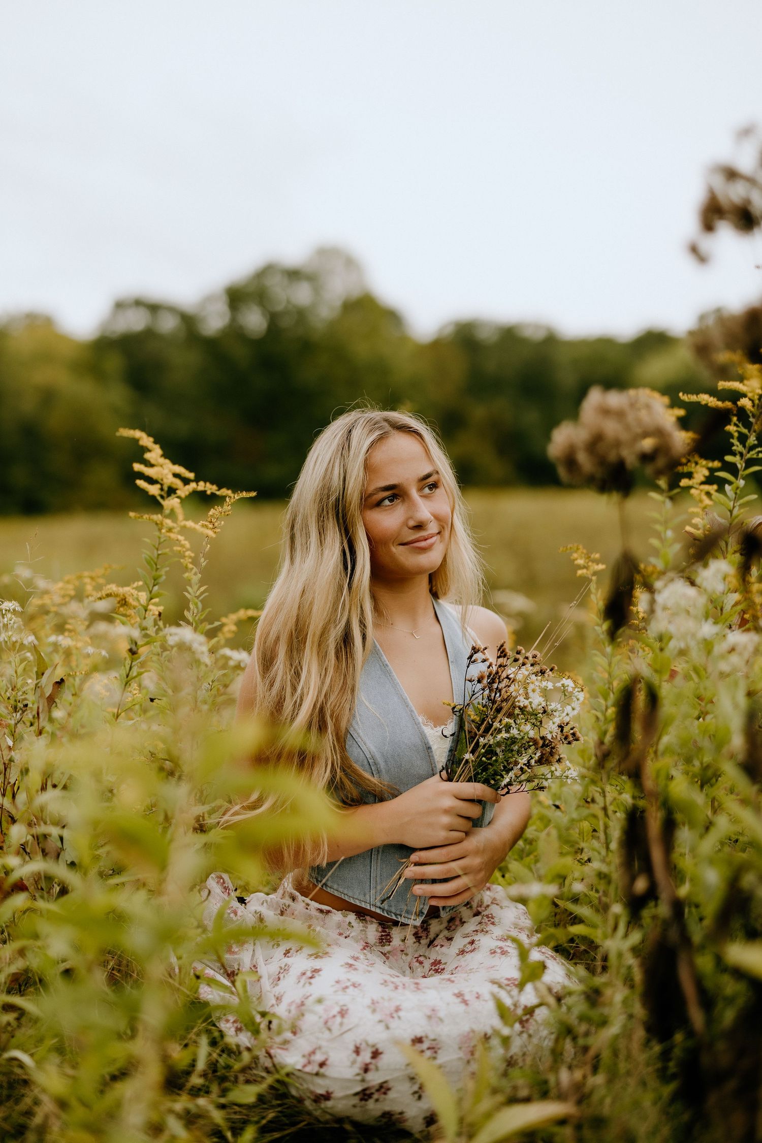 Romantic portrait in golden wildflower field holding dried flowers at sunset.