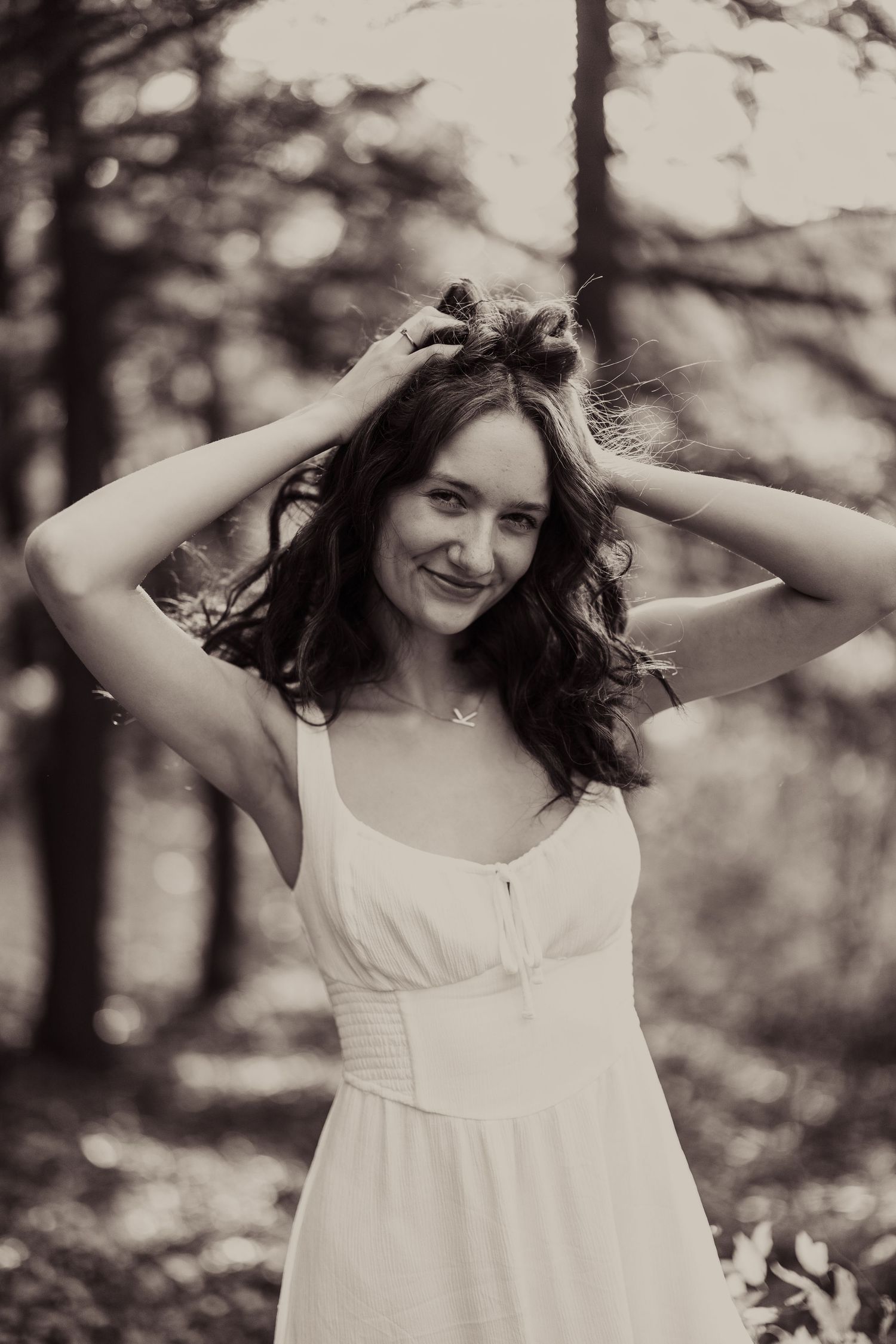 A vintage-style portrait in black and white featuring a white summer dress in a forest setting.