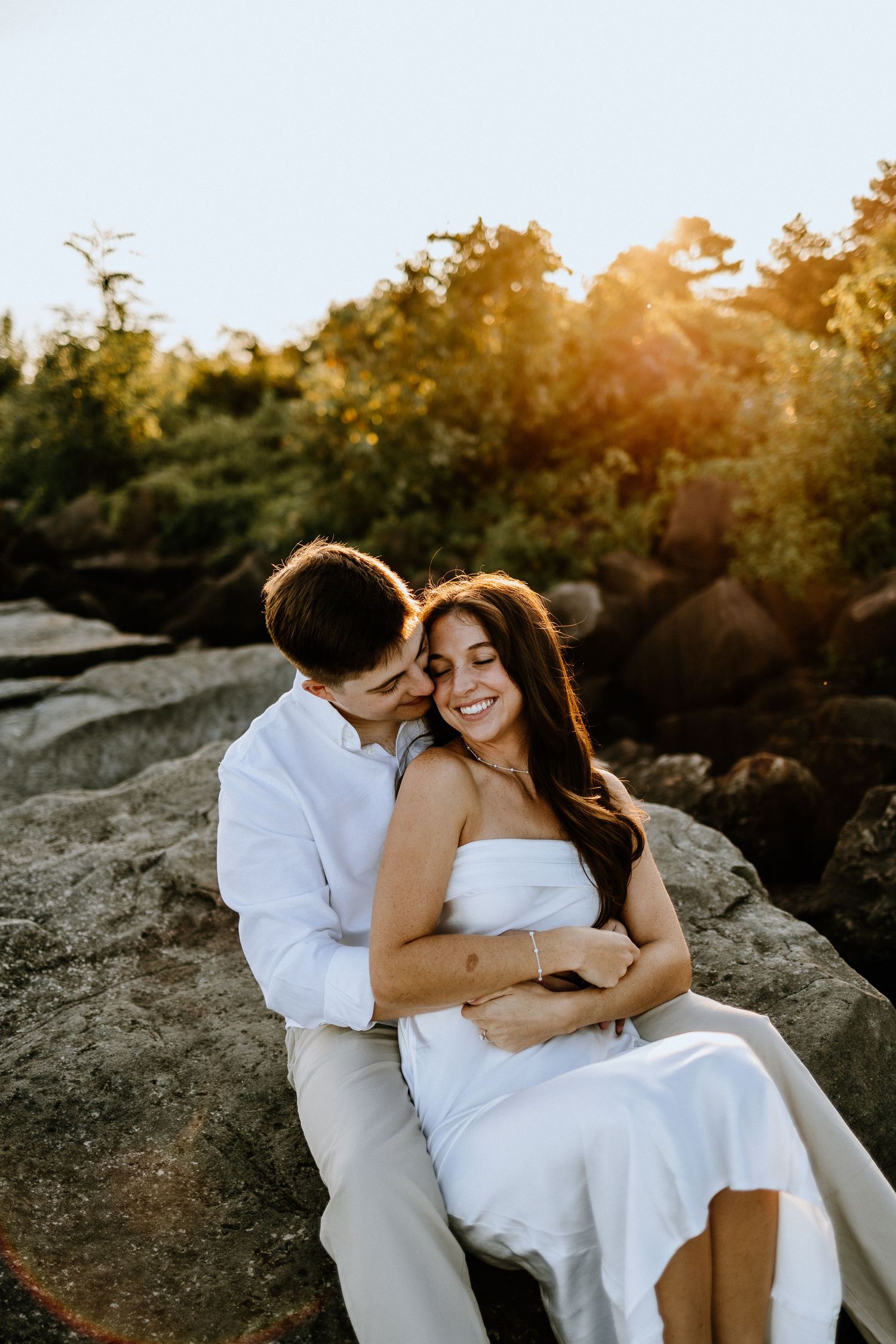 A couple shares an intimate moment on rocky terrain at golden hour.