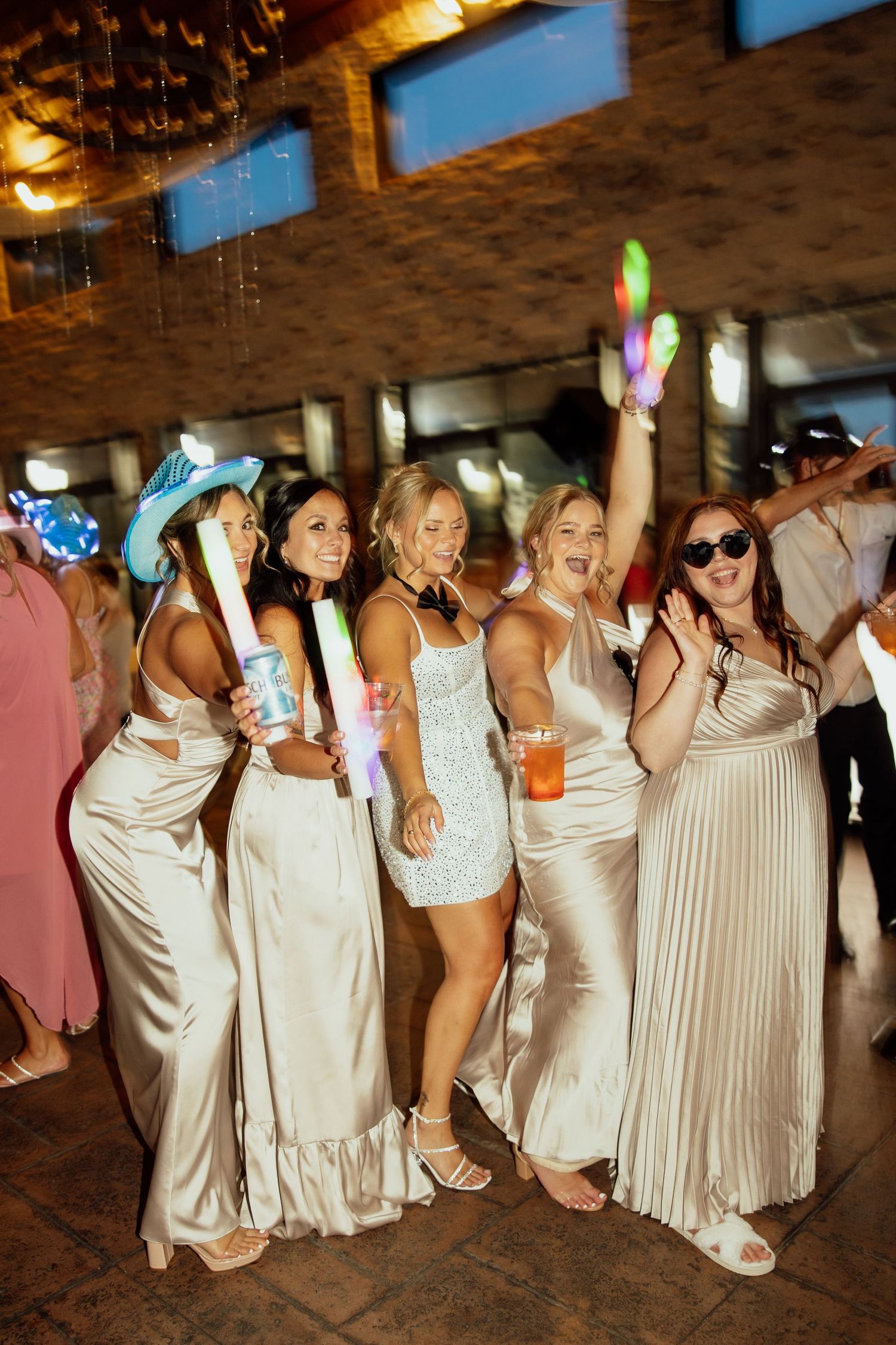 Bridesmaids in cream-colored dresses posing together during a lively wedding reception.