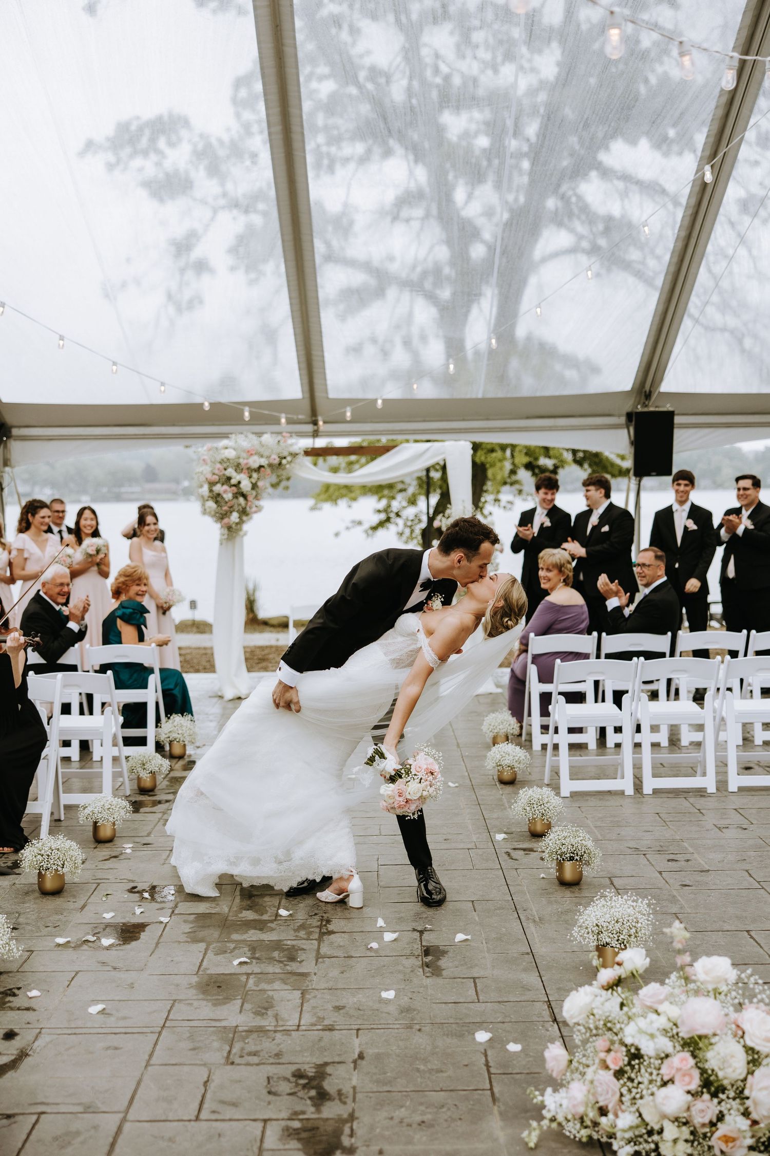 A fun wedding photo sequence showing a couple performing a dip dance move under a white tent with guests watching.