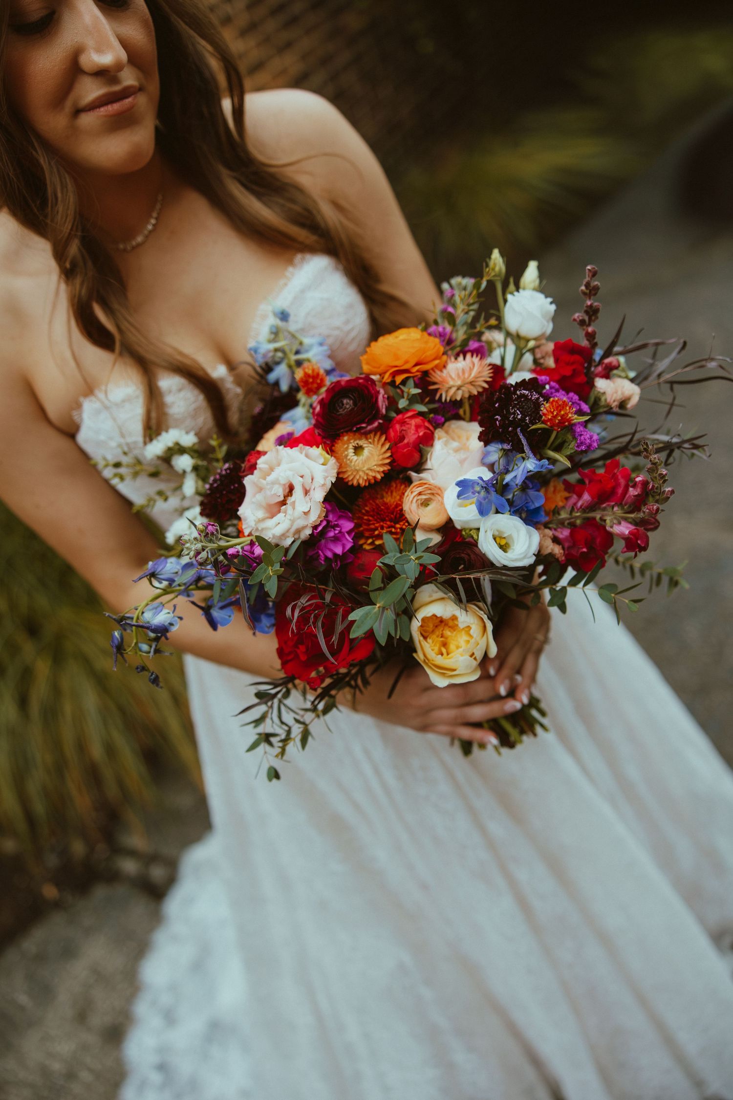 Vibrant bridal bouquet with red, blue, and orange flowers against a white wedding dress.