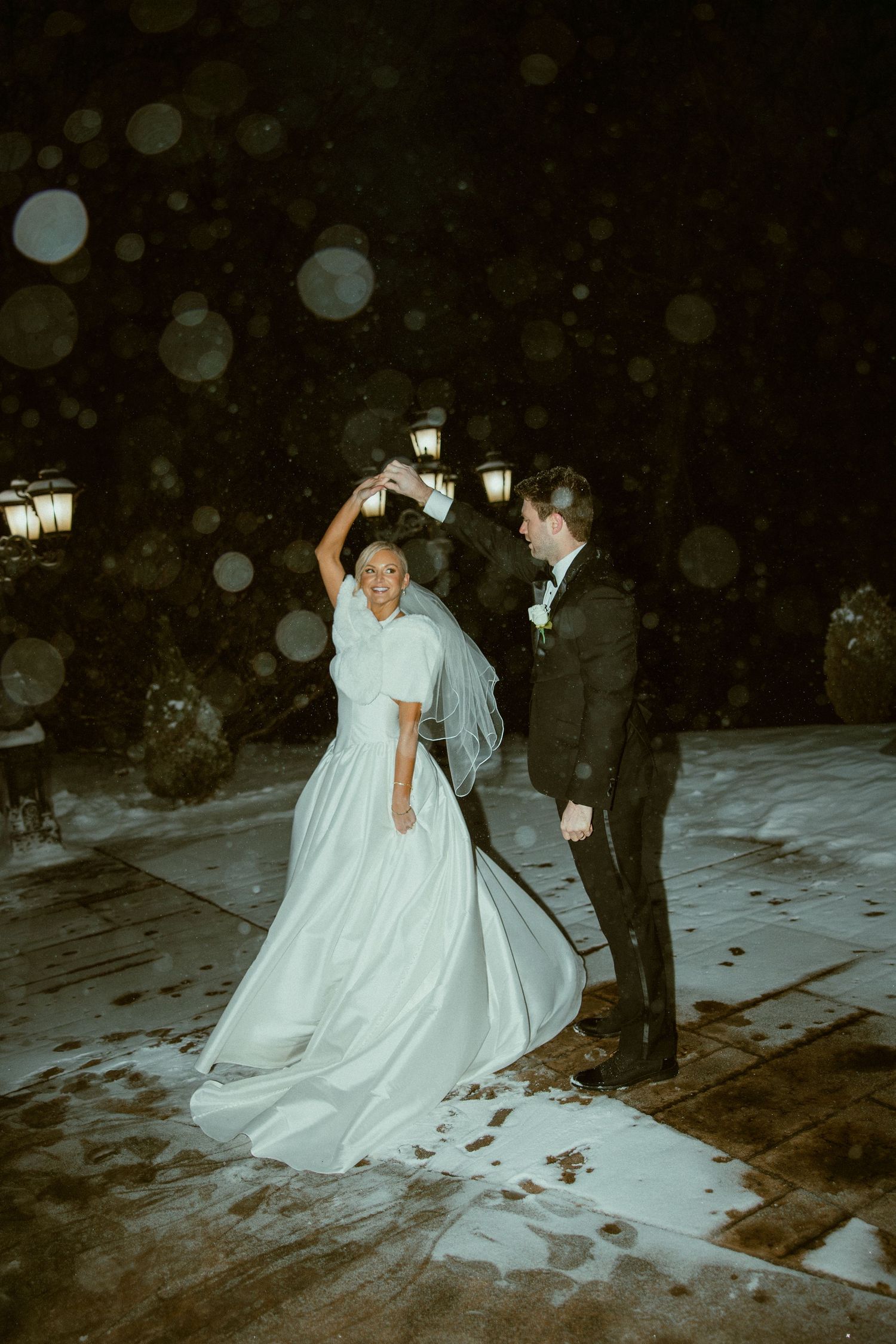 Couple dances in the snow at night with glowing lanterns creating a romantic atmosphere.
