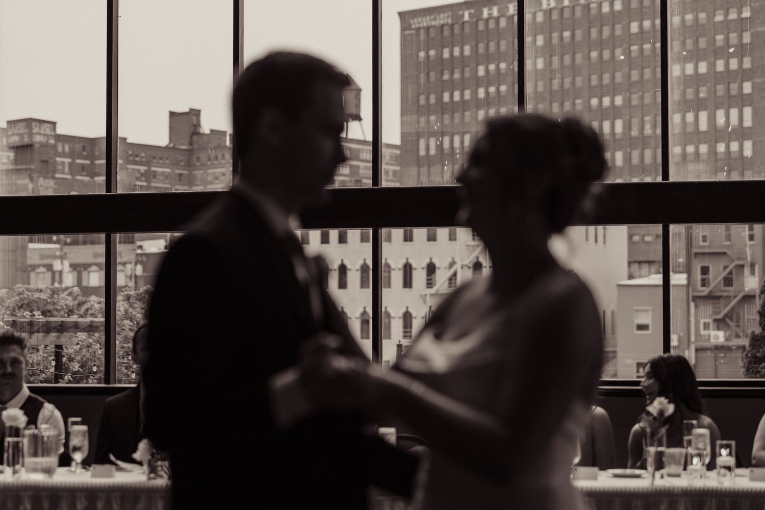 Silhouetted wedding reception scene with city buildings visible through windows.