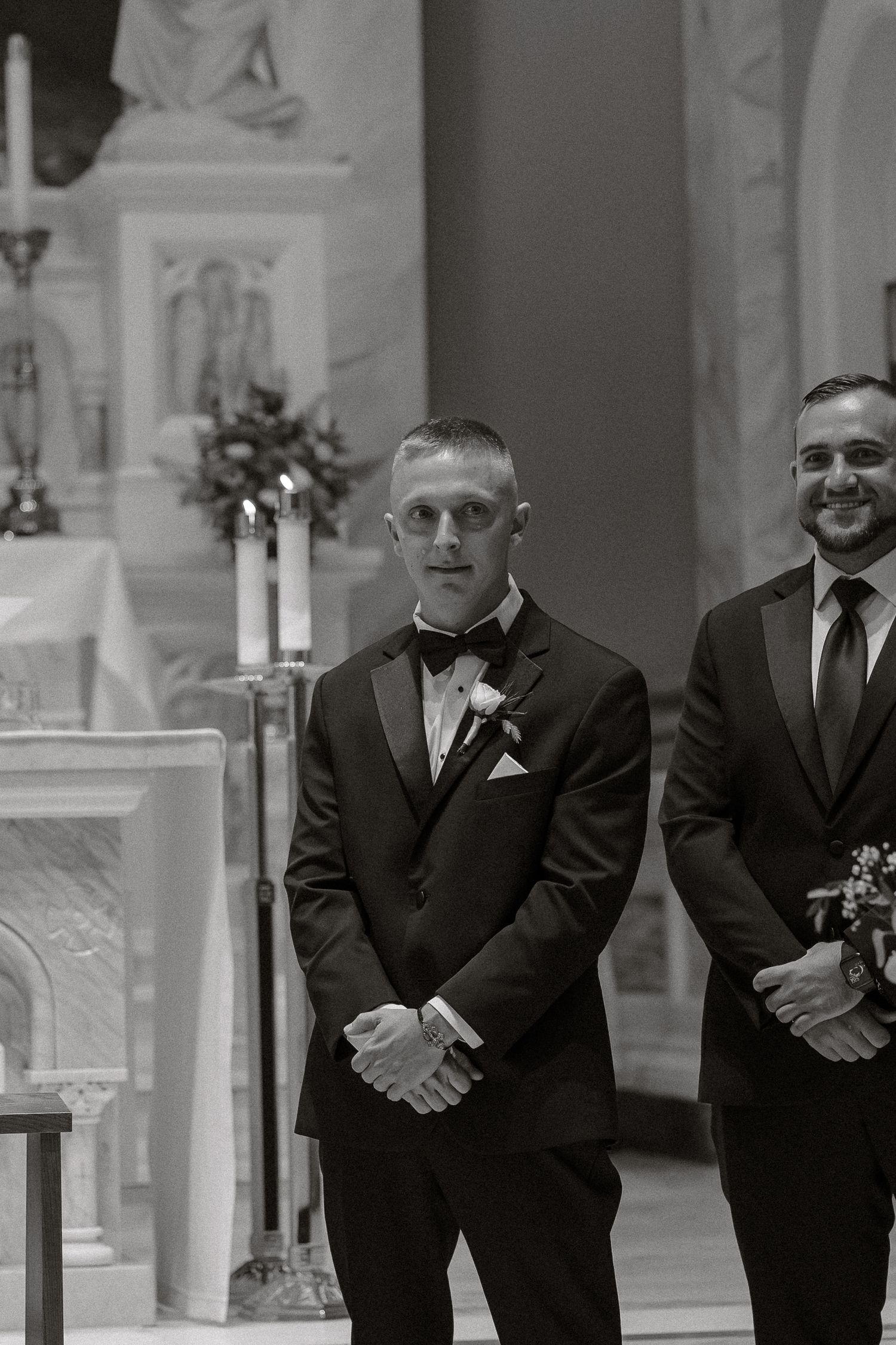 Groomsmen in black suits stand in a line inside an elegant church during a wedding ceremony.