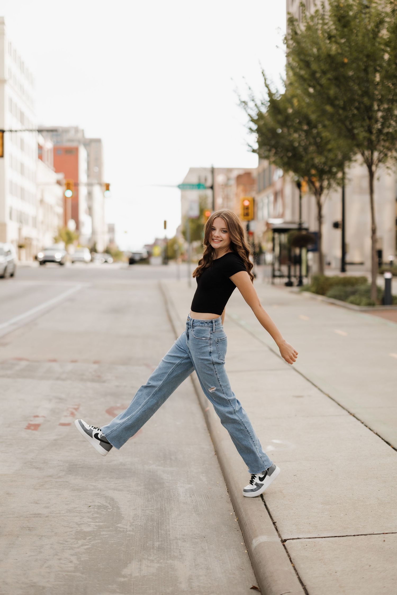 Playful street style photo of someone balancing on a curb in casual denim and sneakers.
