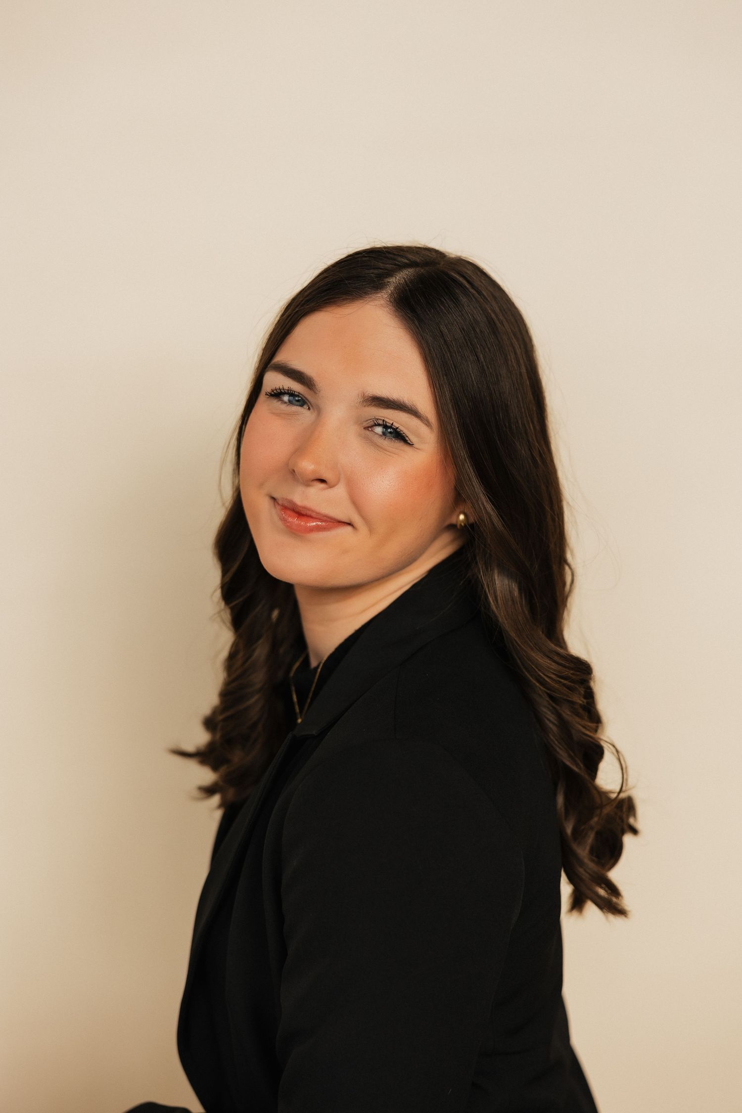 Side profile portrait of person in black blazer against beige background.