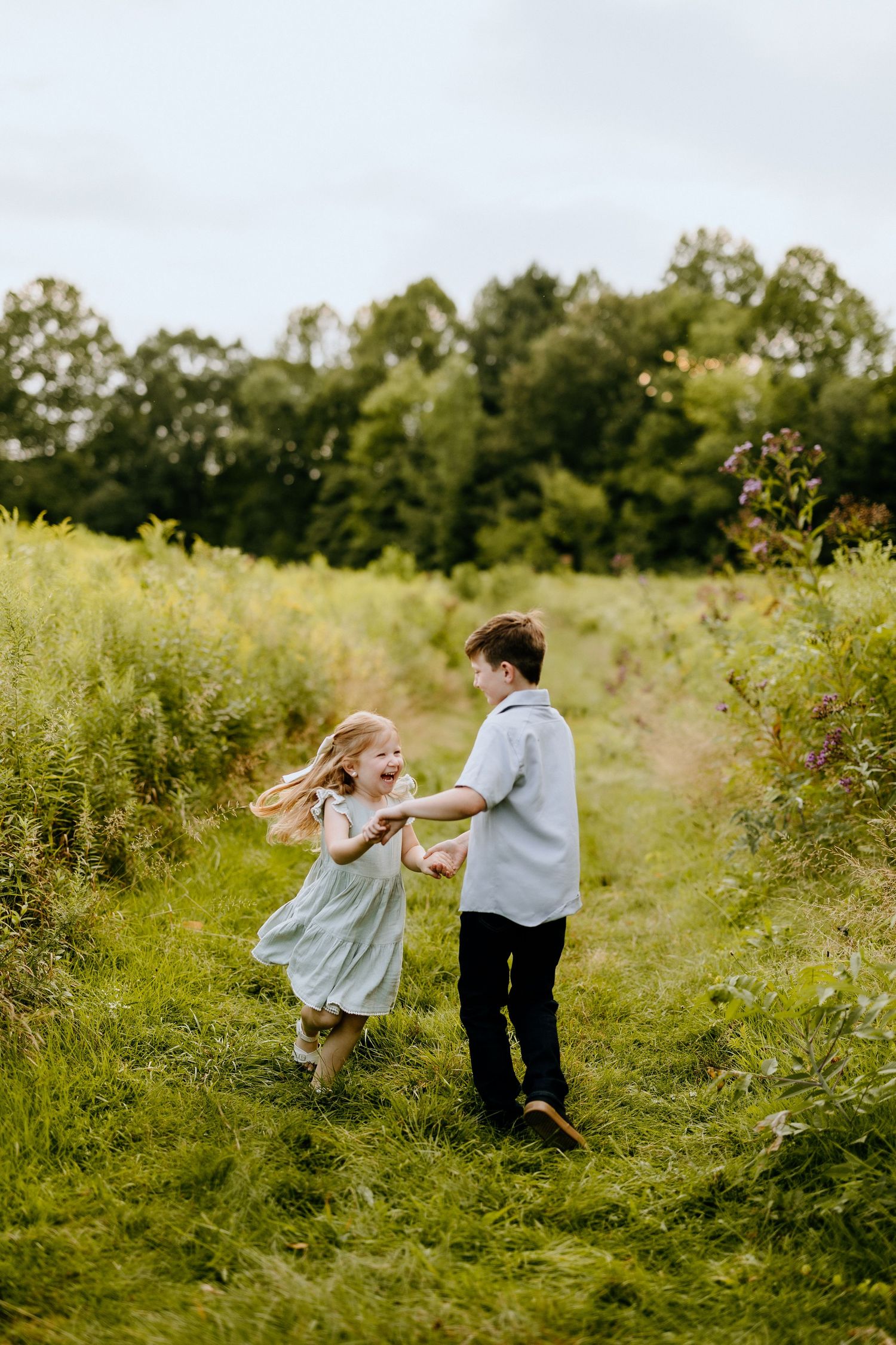 Two children dancing and playing together on a grassy path surrounded by wildflowers.