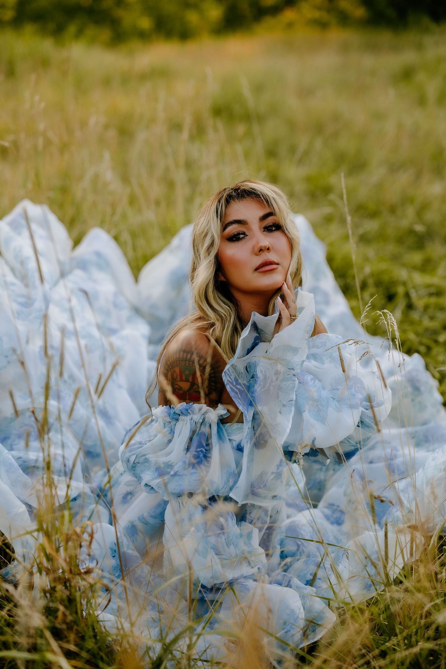 Dreamy outdoor portrait with flowing light blue dress in tall grass field.