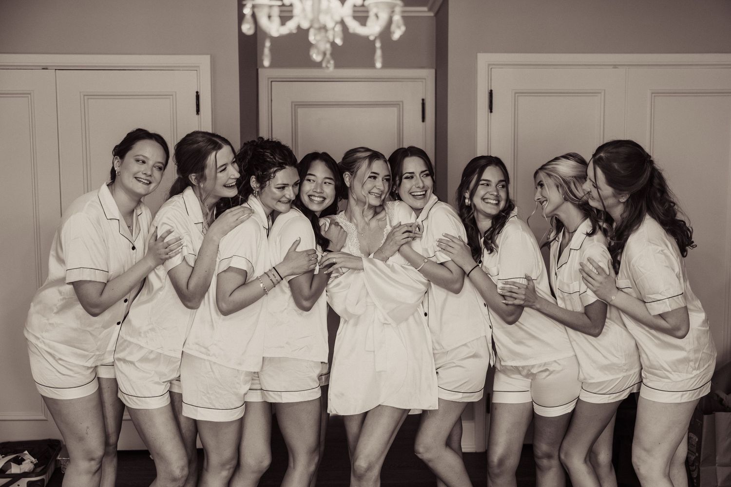 A group of women in matching white robes laughing and posing together in a candid bridal party moment.